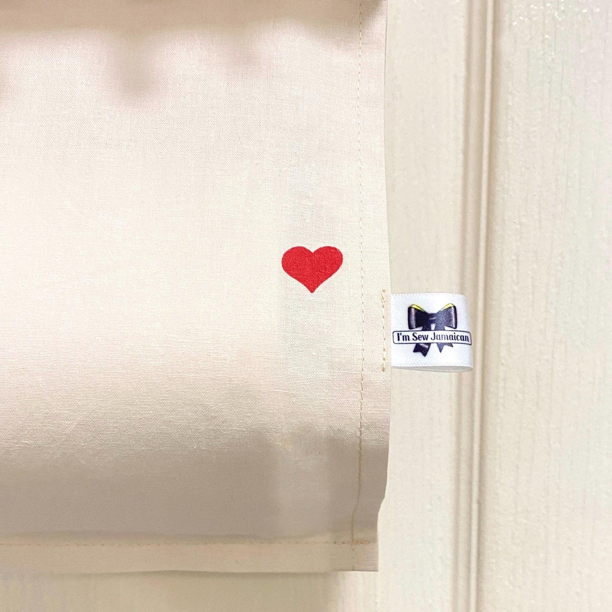 close up neutral cream cotton fabric toilet roll holder with red heart hanging behind the bathroom door, front view.