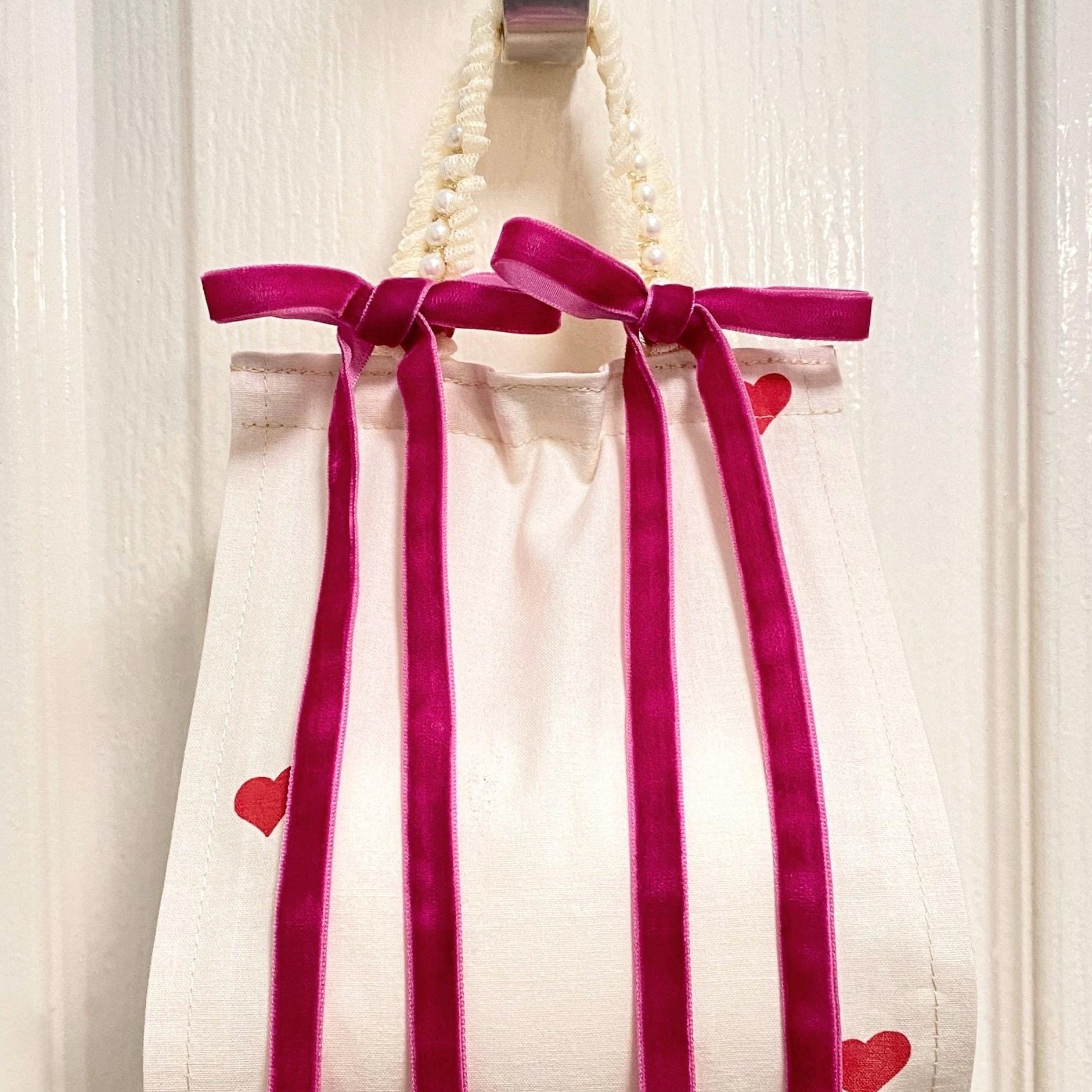 Close up front view of cotton fabric toilet roll holder with hearts hanging behind the bathroom door.