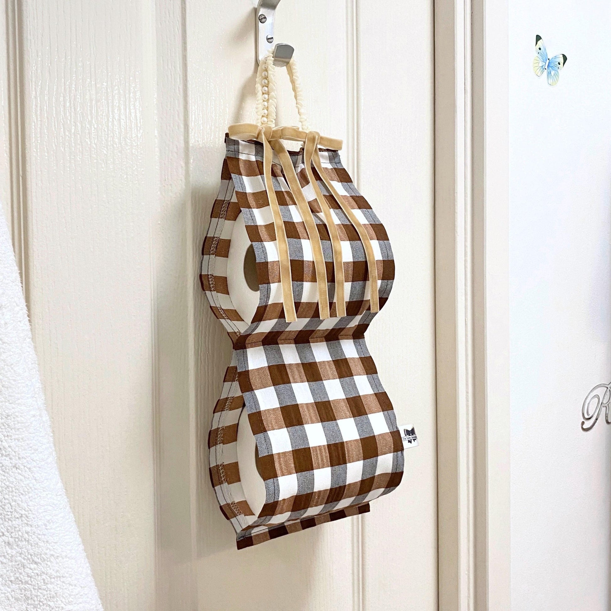 Brown and white gingham fabric toilet roll holder hanging in a bathroom.