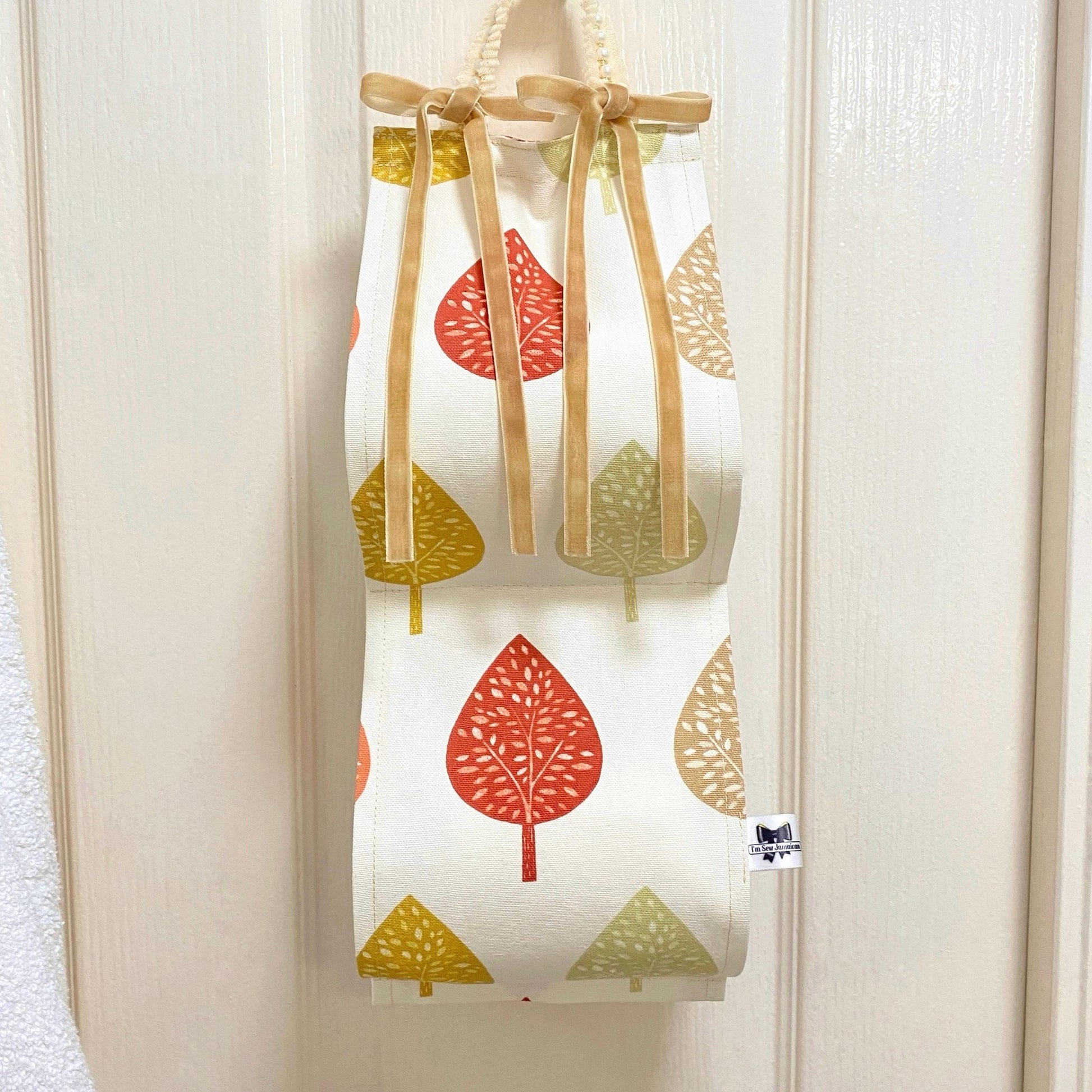 Earthy-coloured cotton fabric toilet roll holder with leaves, hanging in a stylish bathroom front view.
