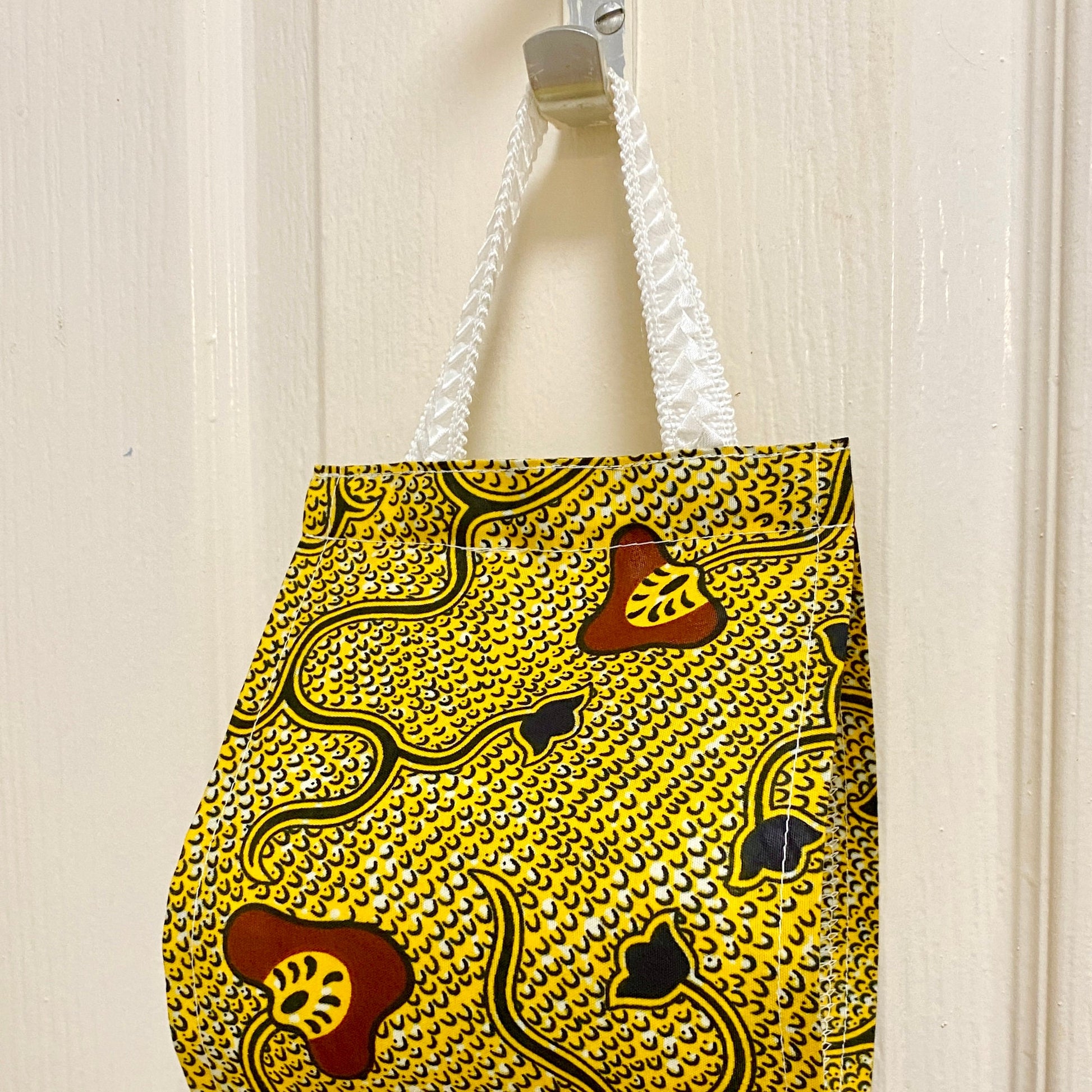 Close up of handle of African wax print cotton toilet roll holder in yellow and black with mushroom and flower motifs in bathroom.