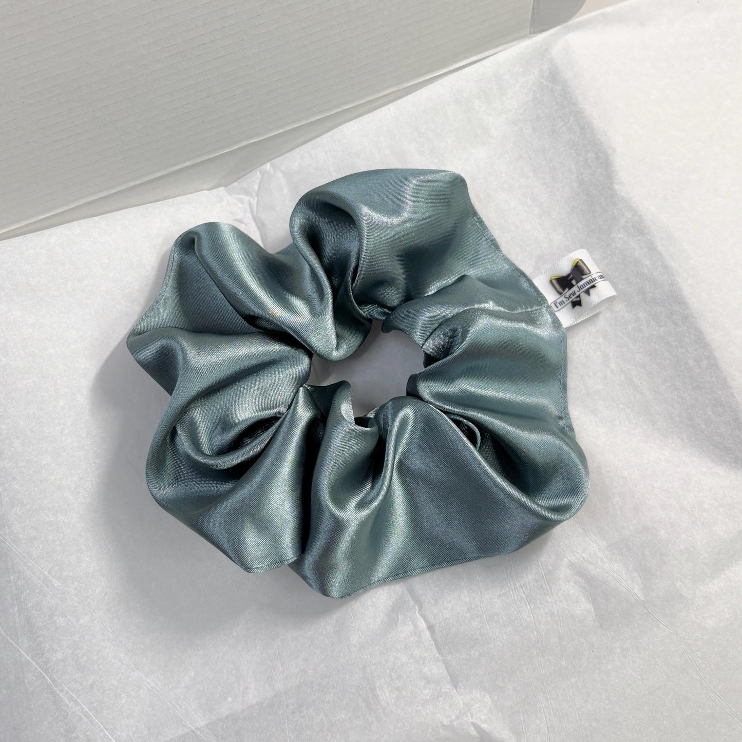Aqua satin hair scrunchie with shine, stylish accessory for all hair types on white tissue paper on carboard box packaging.