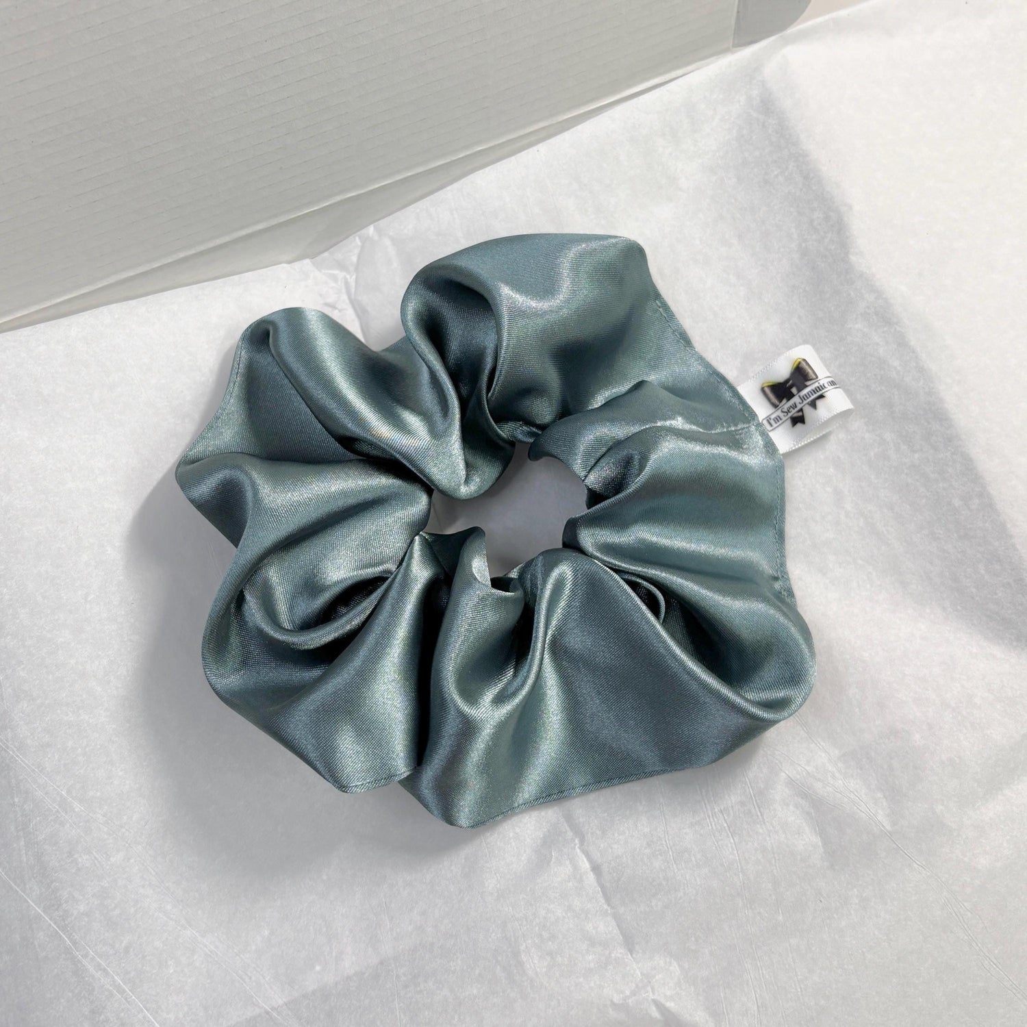 Aqua satin hair scrunchie with shine, stylish accessory for all hair types on white tissue paper on carboard box packaging.