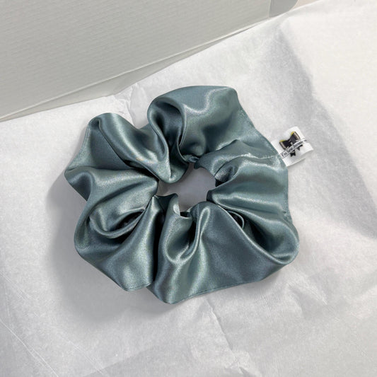 Aqua satin hair scrunchie with shine, stylish accessory for all hair types on white tissue paper on carboard box packaging.