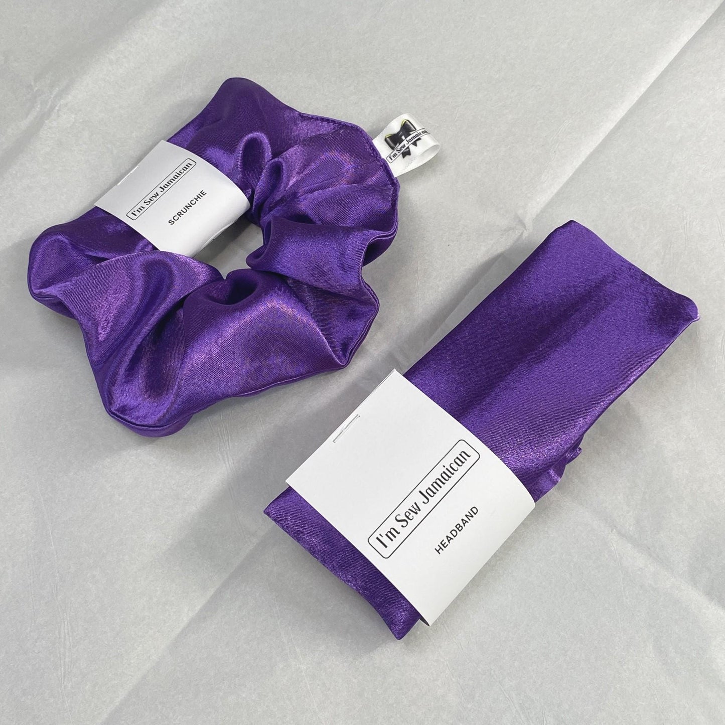 Purple satin headband and satin hair scrunchie displayed on white tissue paper.