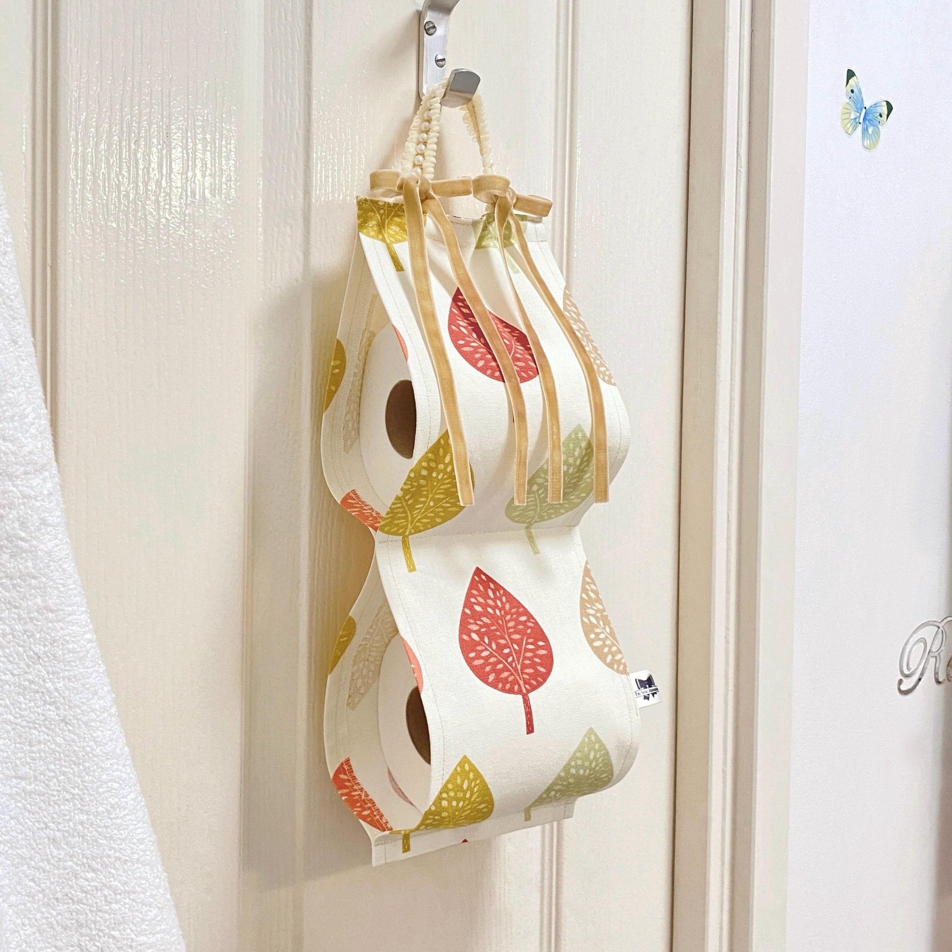 Earthy-coloured cotton fabric toilet roll holder with leaves, hanging in a stylish bathroom for a natural, rustic touch.