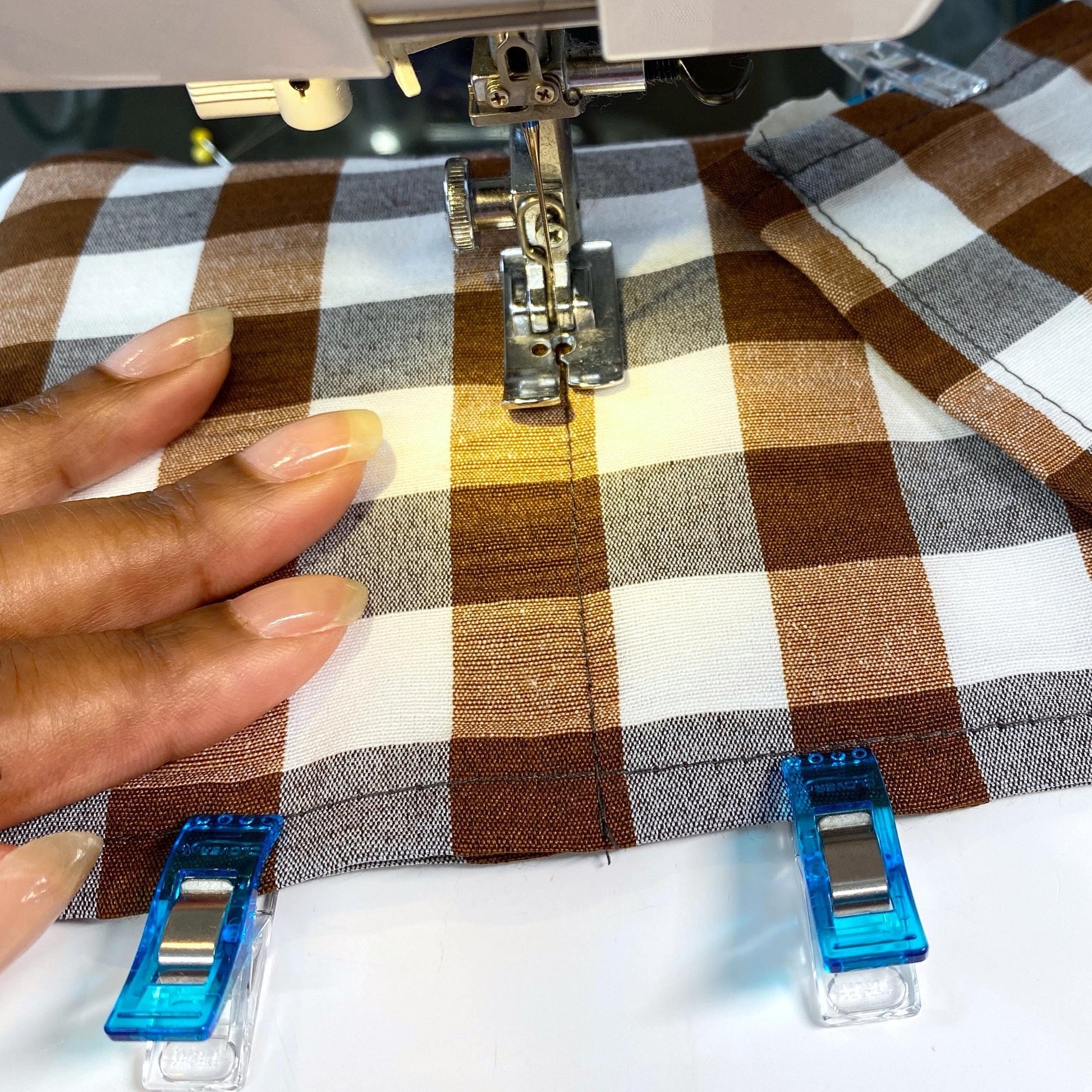 Close-up of a sewing machine stitching a brown and white gingham fabric toilet roll holder with the needle in focus.