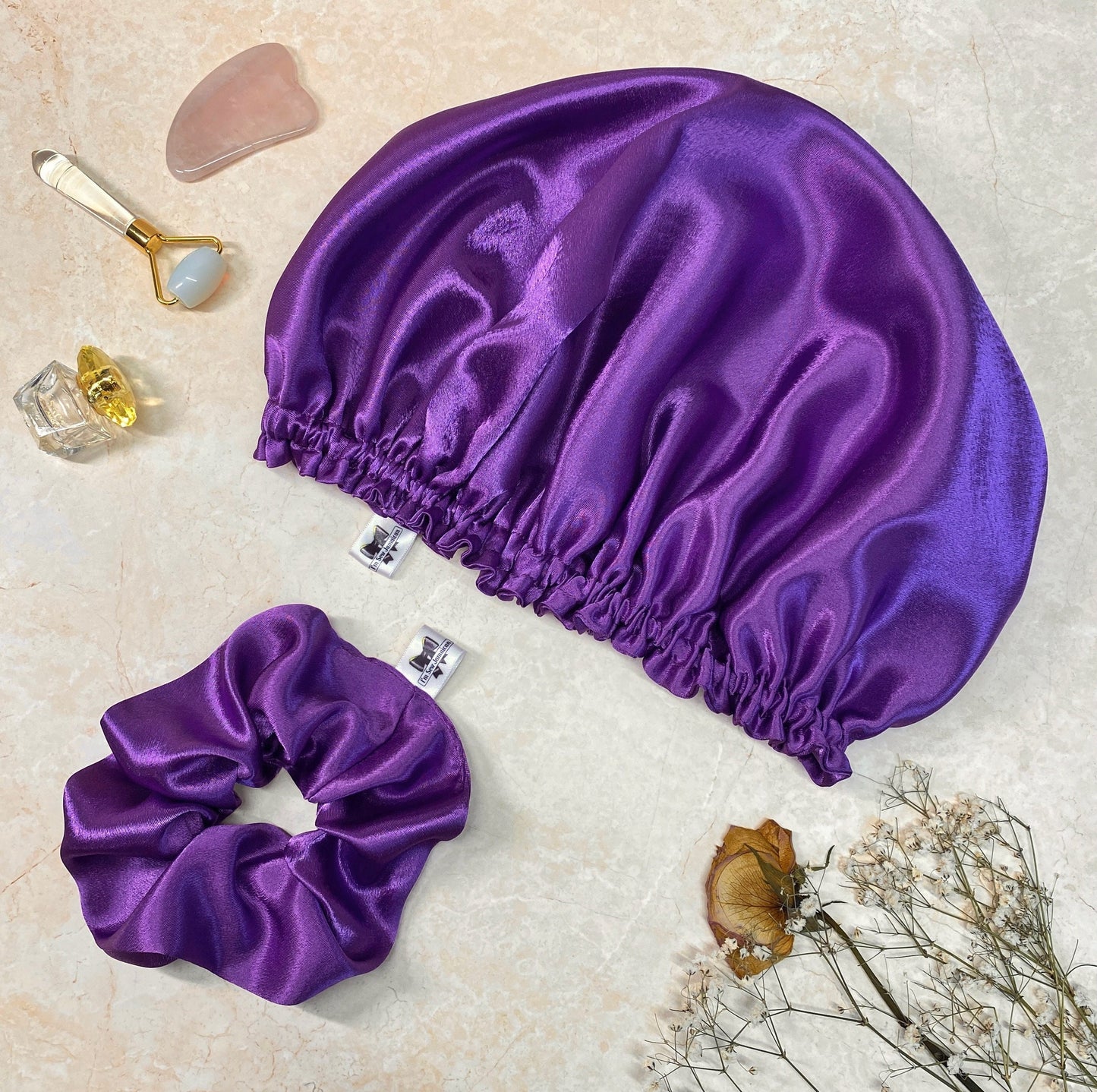 Purple satin hair bonnet and hair scrunchie gift set in purple on marble background.