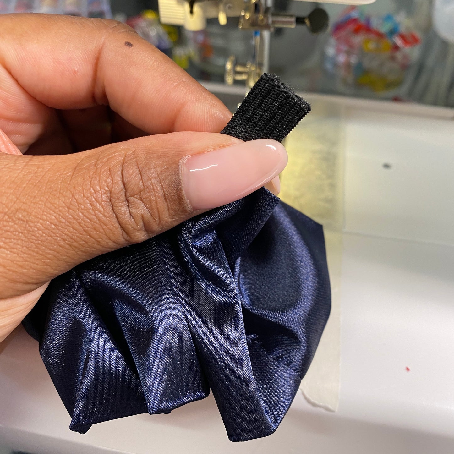 A woman's hand holding navy blue satin fabric and elastic in front of sewing machine.