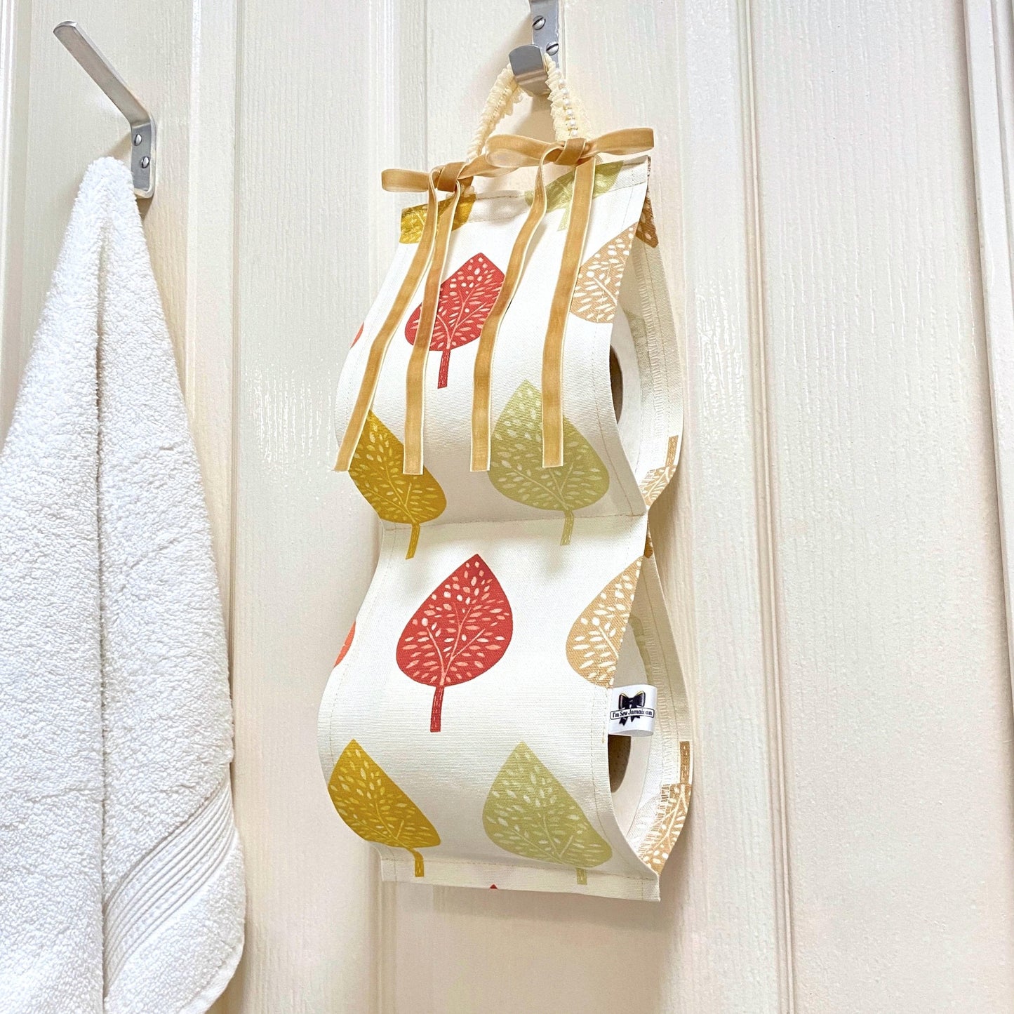 Earthy-coloured cotton fabric toilet roll holder with leaves, hanging in a stylish bathroom for a natural, rustic touch.