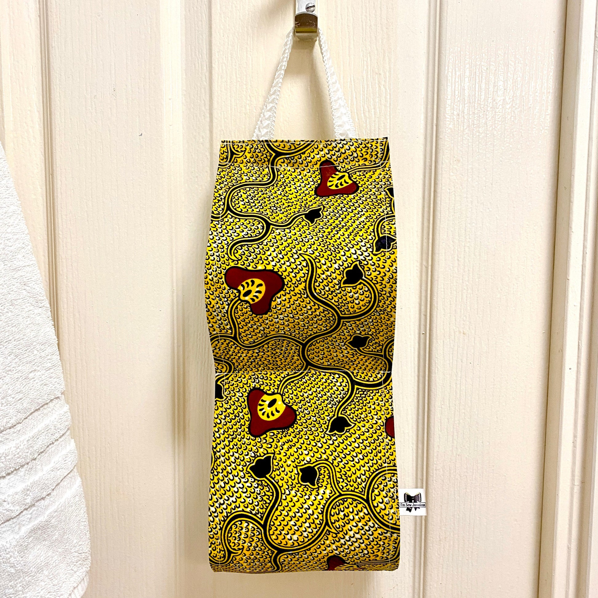 African wax print cotton toilet roll holder in yellow and black with mushroom and flower motifs, hanging in a bathroom front view.