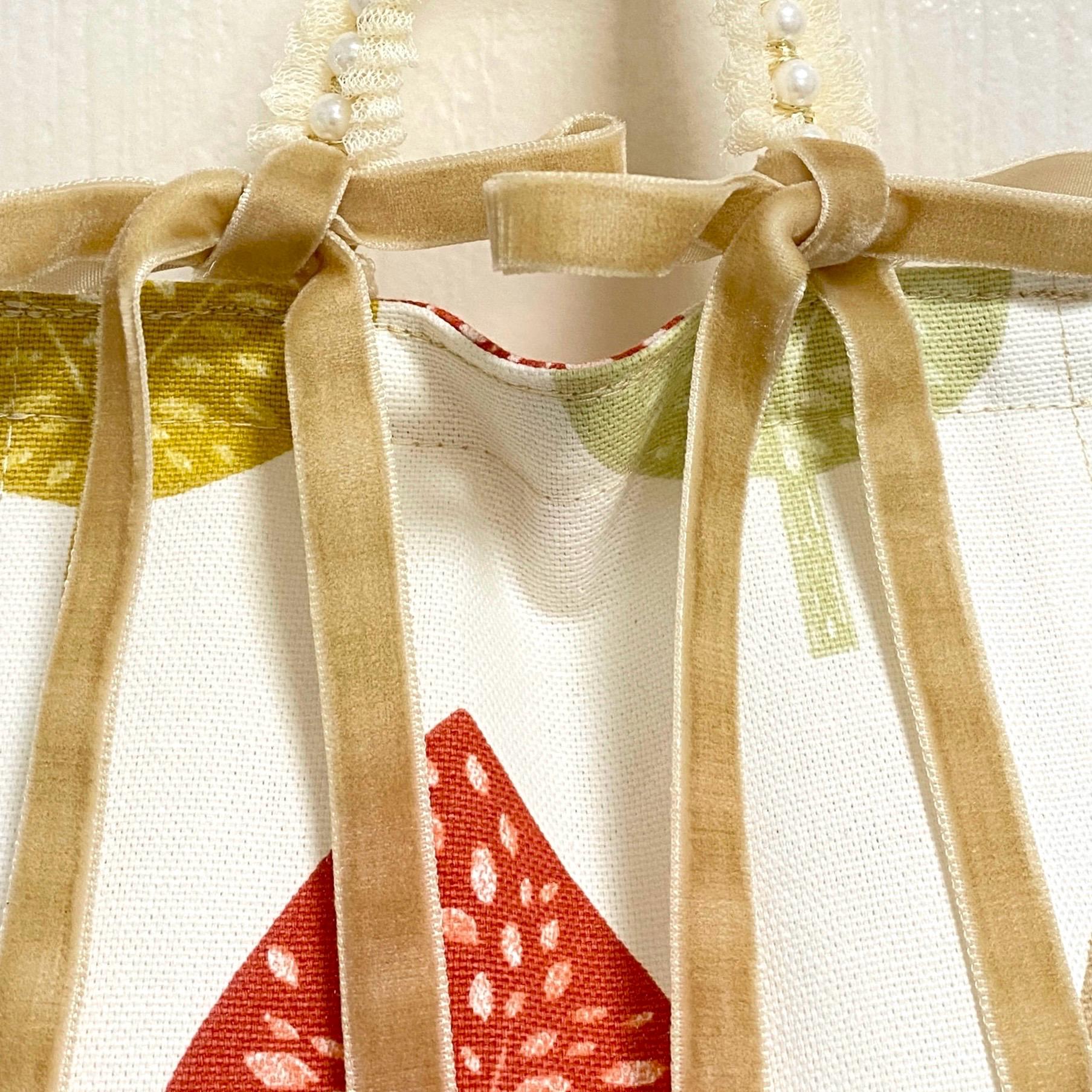 Close up earthy-coloured cotton fabric toilet roll holder with velvet bows hanging in a bathroom.