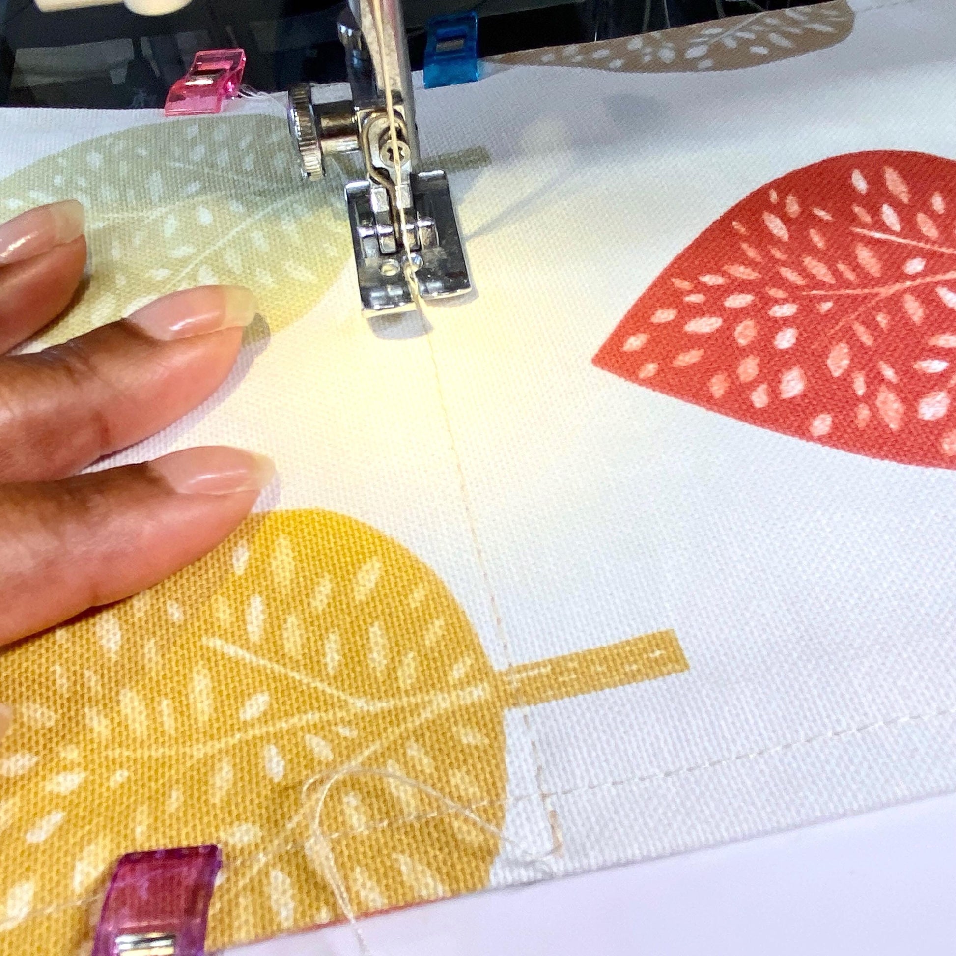 Close-up of a sewing machine stitching a earthy-coloured leaf fabric toilet roll holder with the needle in focus.