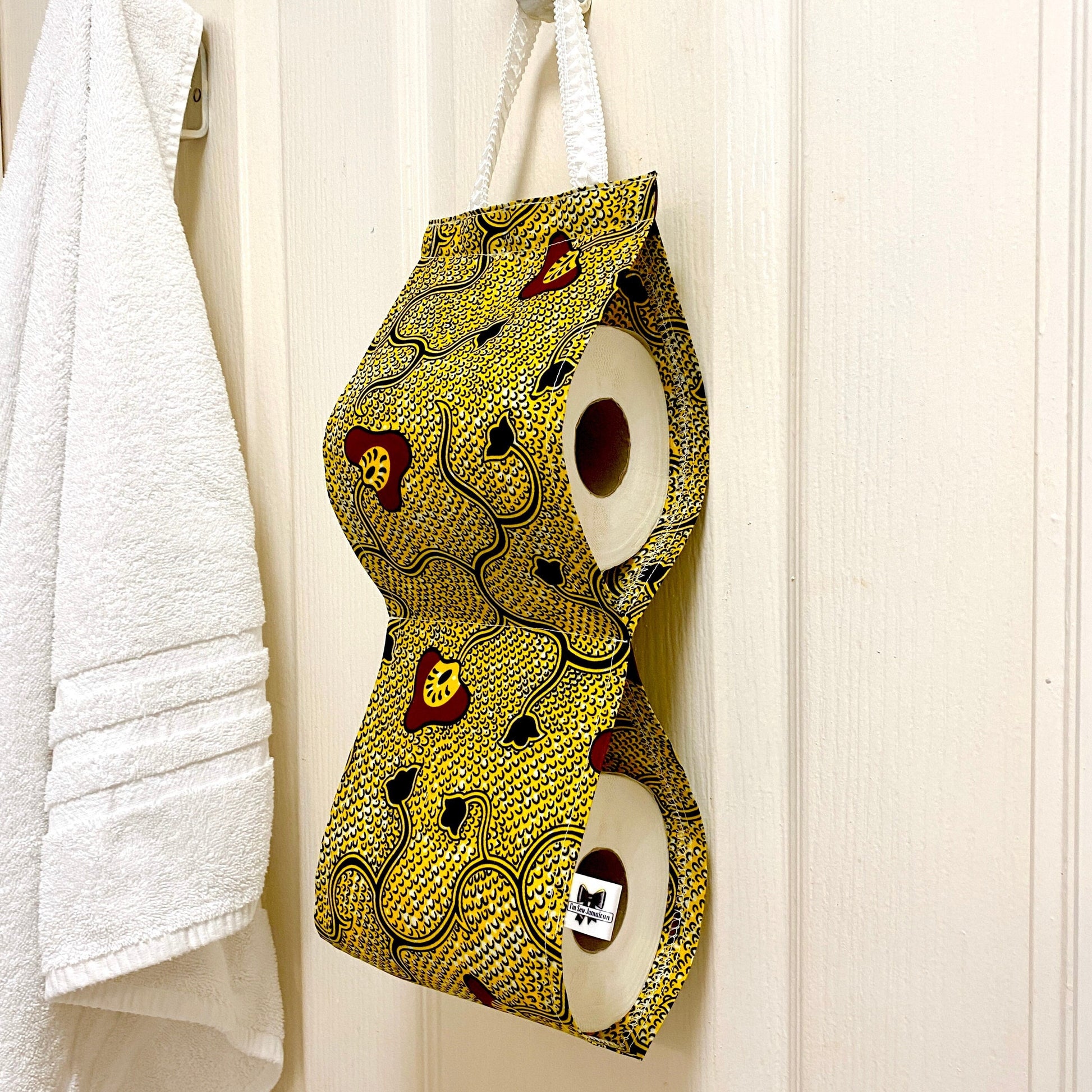 African wax print cotton toilet roll holder in yellow and black with mushroom and flower motifs, hanging in a bathroom side view.