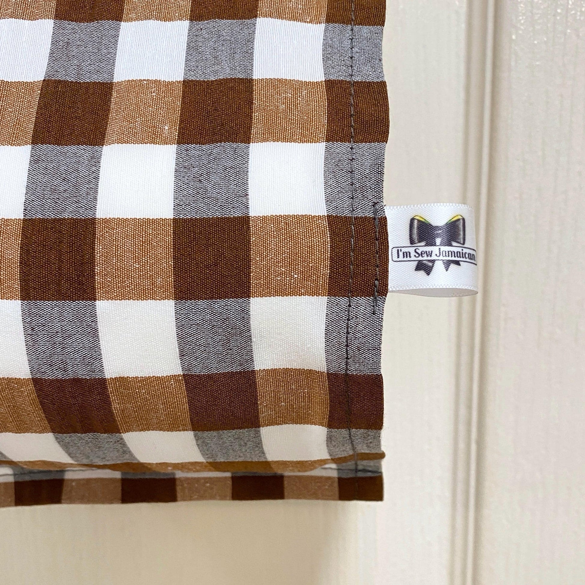 close up brown and white gingham fabric toilet roll holder hanging in a bathroom setting.