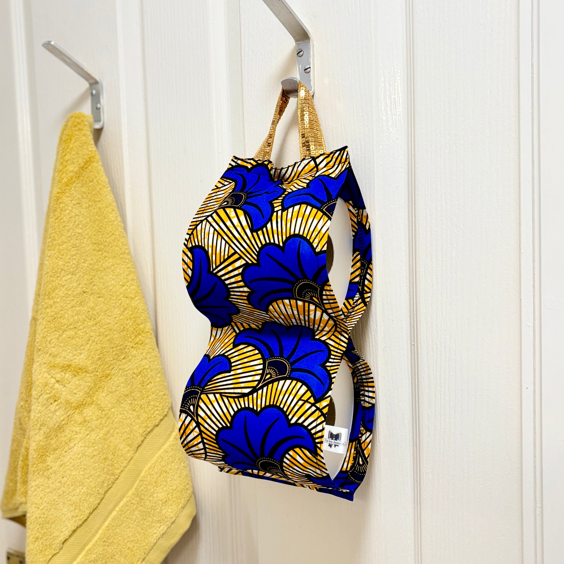 Blue and yellow floral print fabric toilet roll holder for 2 rolls, hanging in a bathroom setting with yellow hand towel.