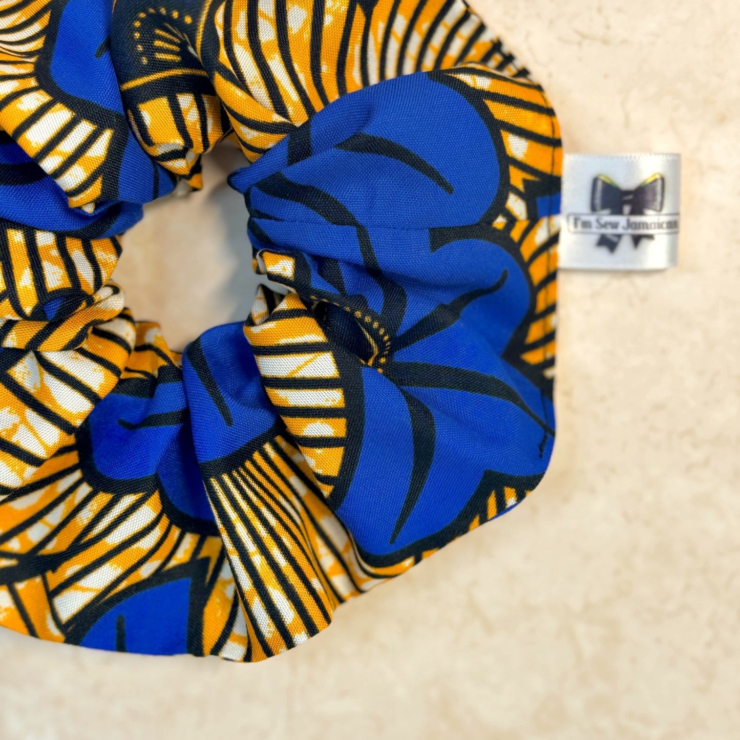 Close up of floral African print blue and yellow scrunchie displayed on marble background.