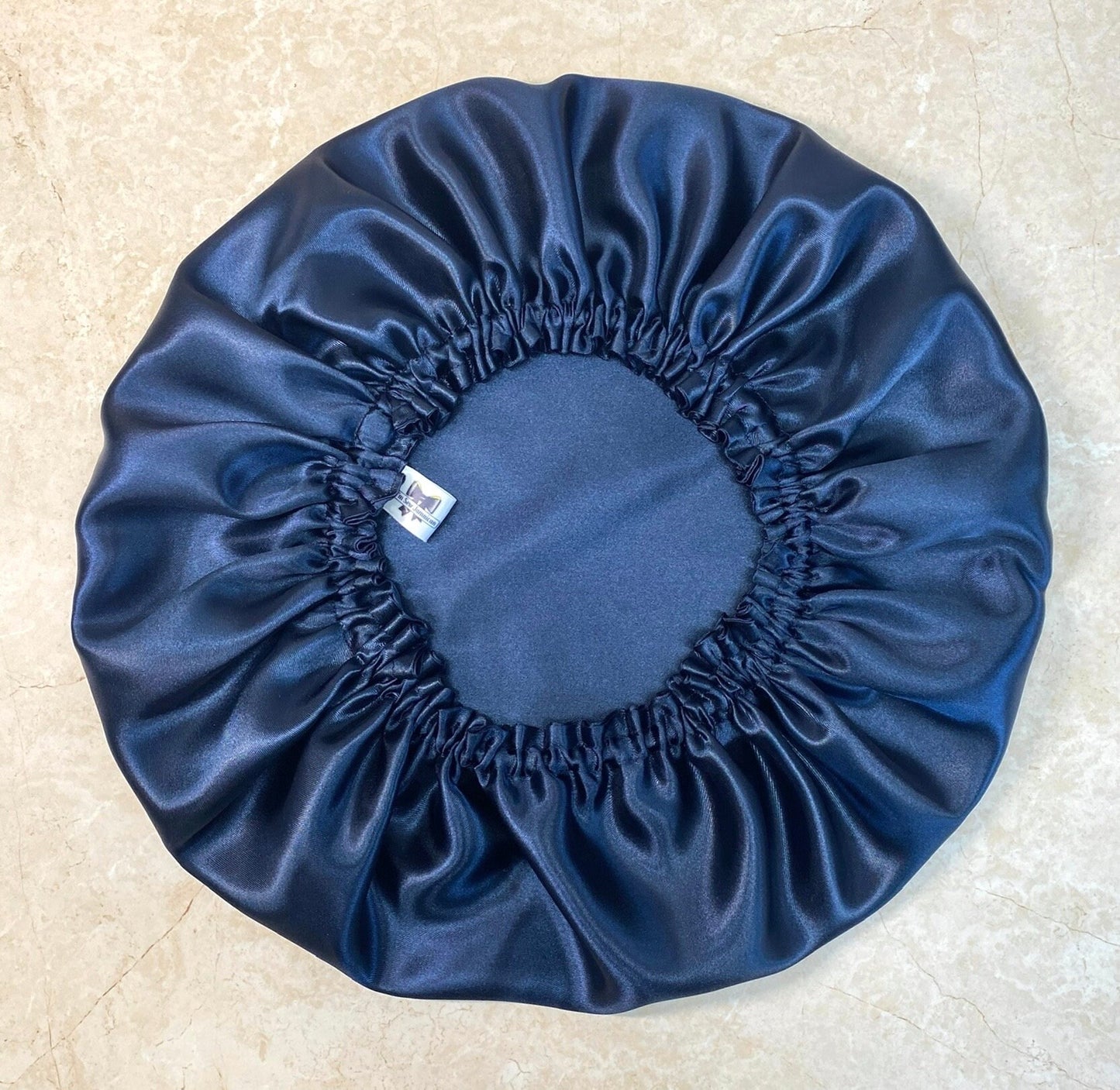 Navy blue satin hair bonnet for protecting hair, displayed on a marble background.