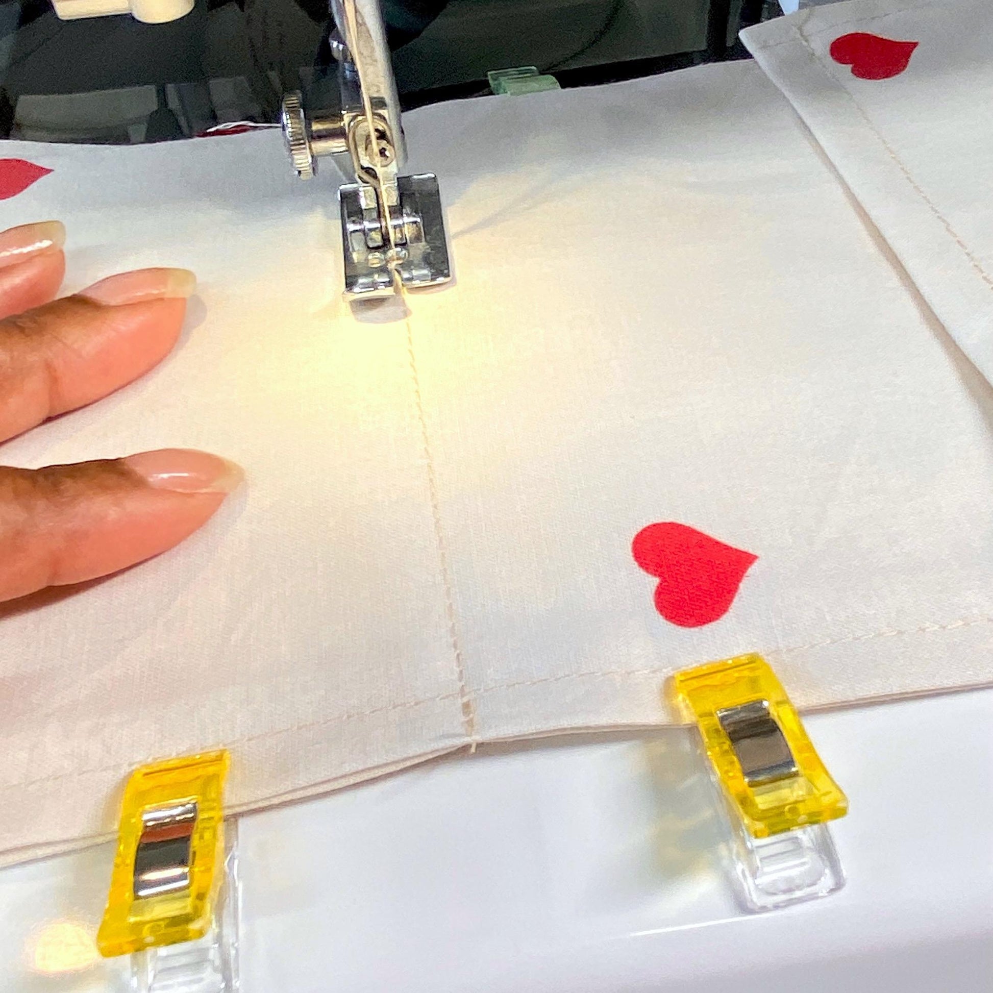 Close-up of a sewing machine stitching cotton fabric toilet roll holder with hearts, needle in focus.
