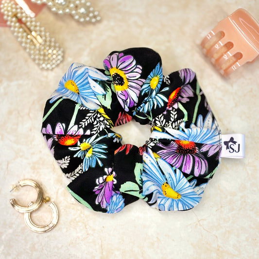 Black floral fabric scrunchie featuring colourful daisy and wildflower print, soft and stylish hair accessory.