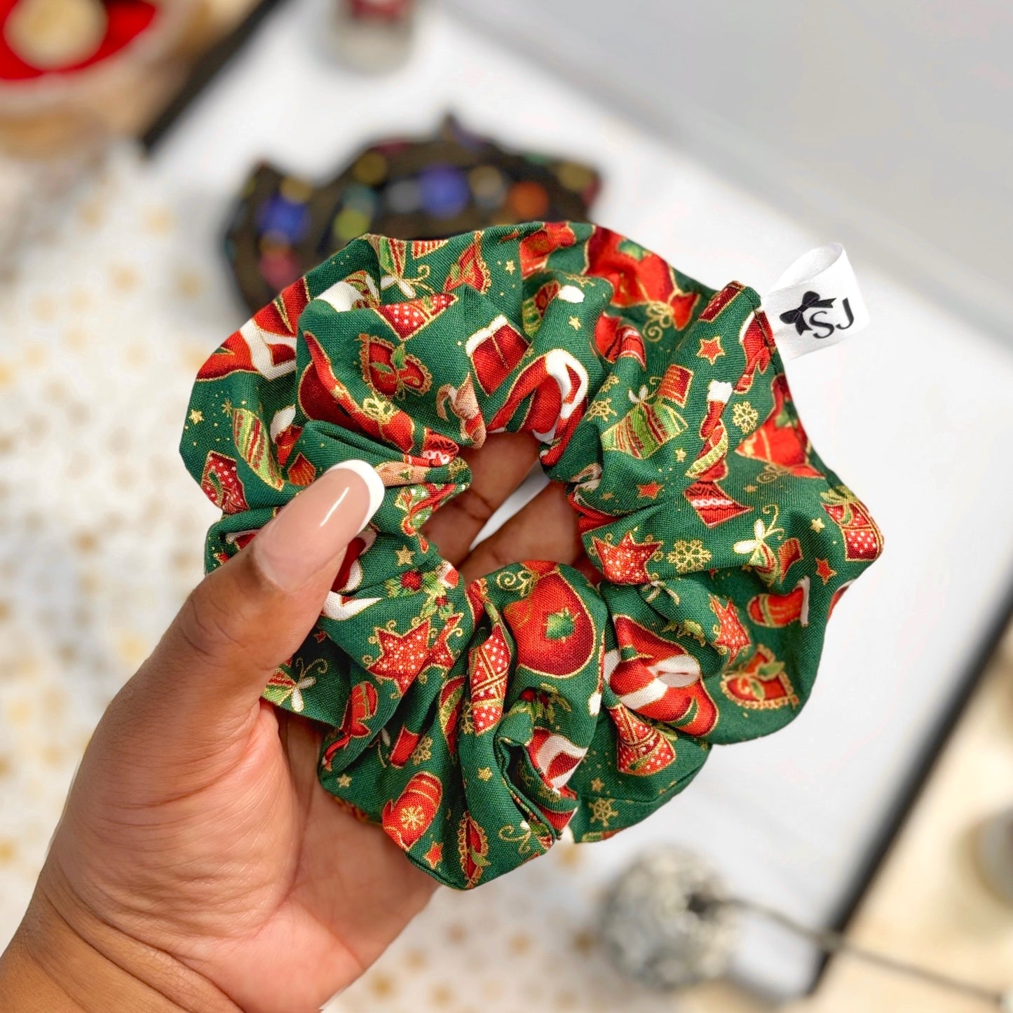 Hand holding a green Festive Christmas scrunchie with festive pattern on a blurred background