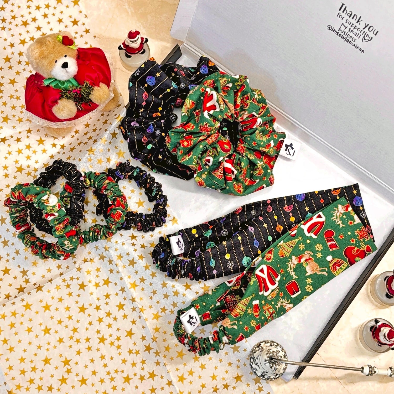 Collection of Christmas-themed hair scrunchies and headbands in a gift box with a teddy bear and small figurines.