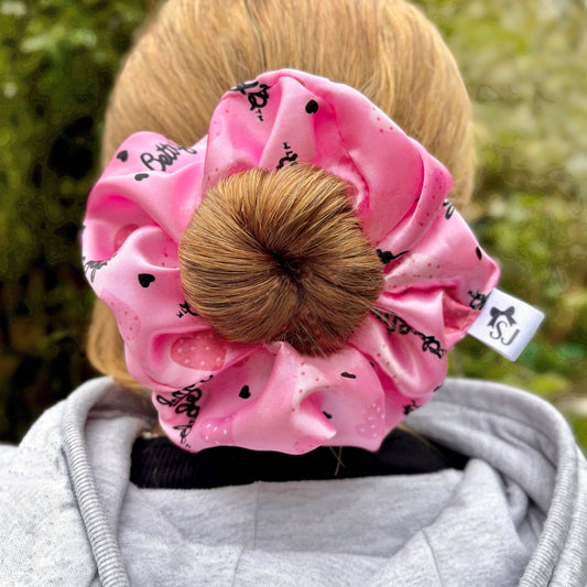 Pink Betty Boop satin scrunchie in a woman's blonde hair from the back, in front of a bamboo tree outside.