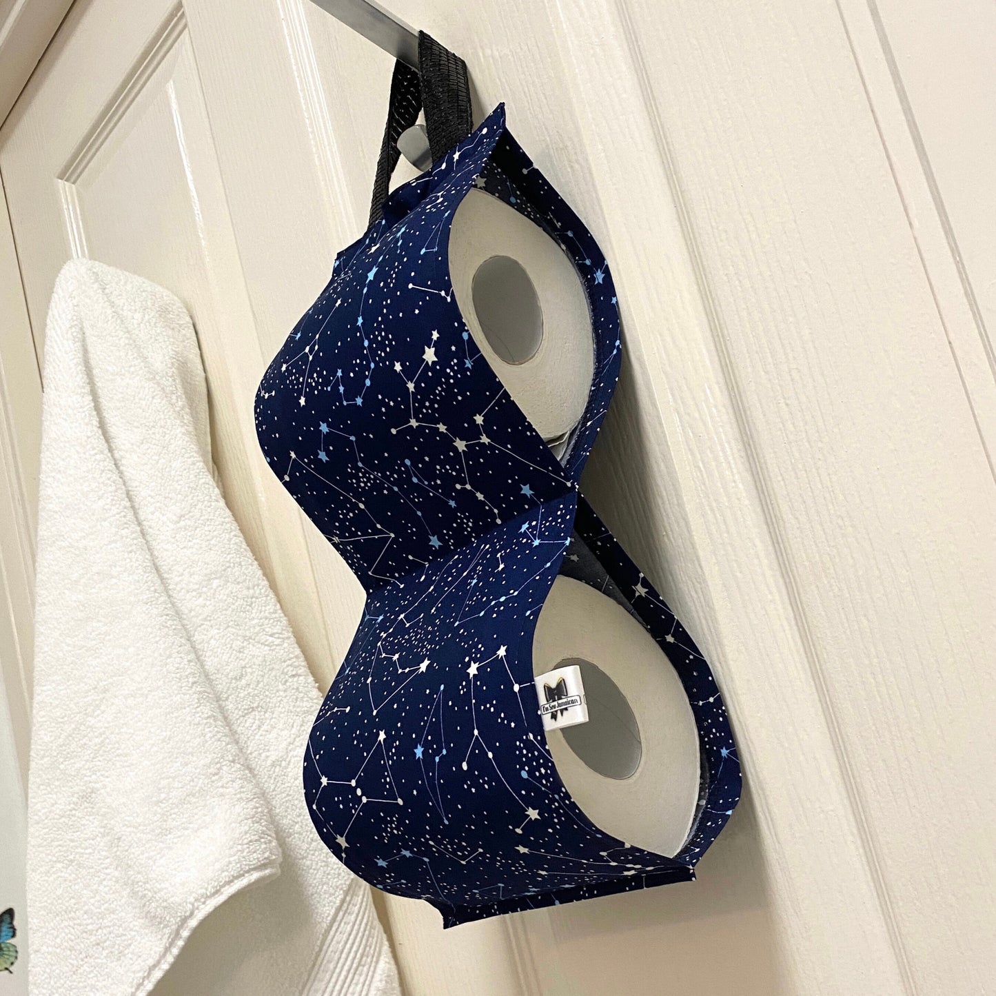 Navy blue night sky fabric toilet roll holder for 2 rolls, hanging in a bathroom setting behind door.