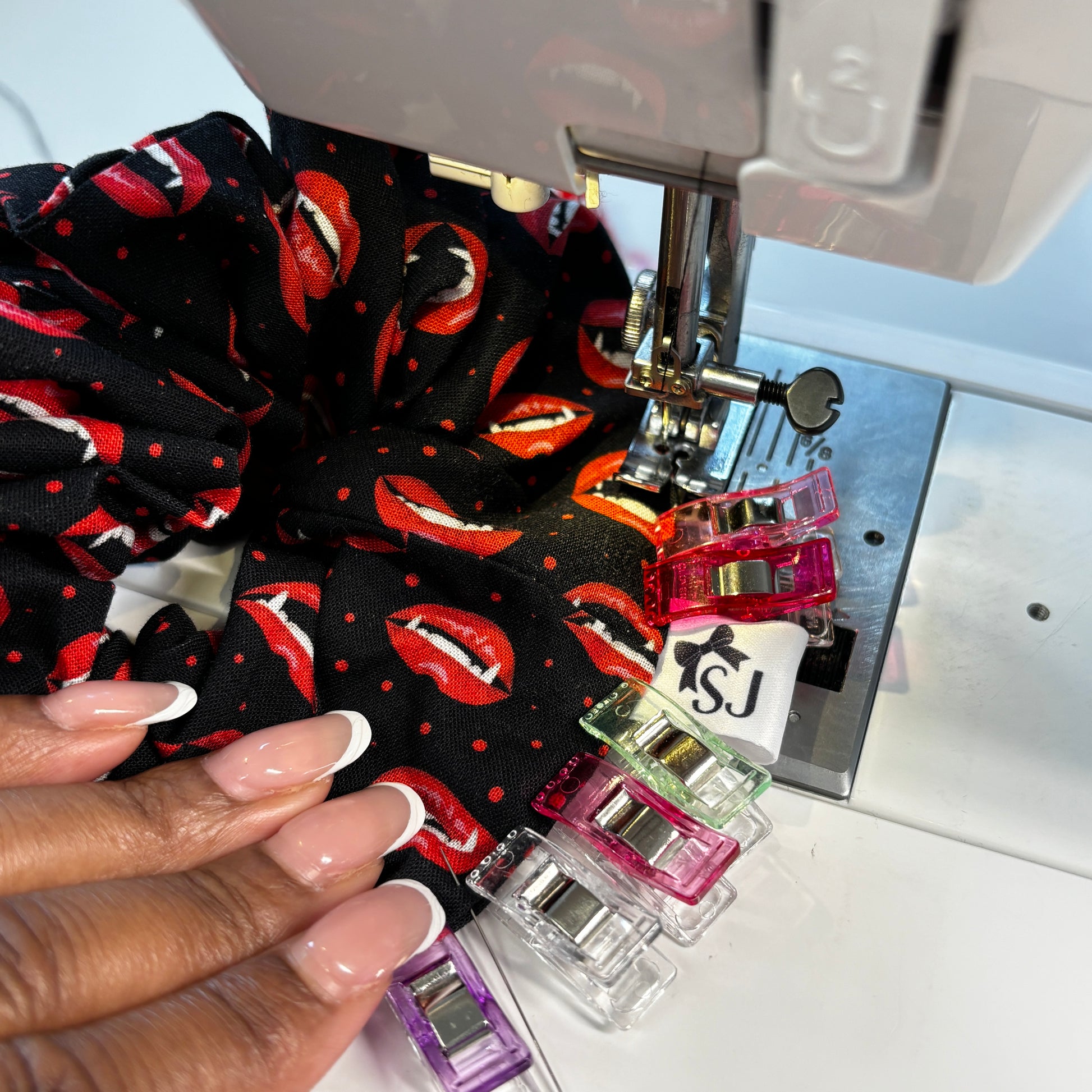 Sewing machine with fabric featuring red lip prints and a hand guiding the material.