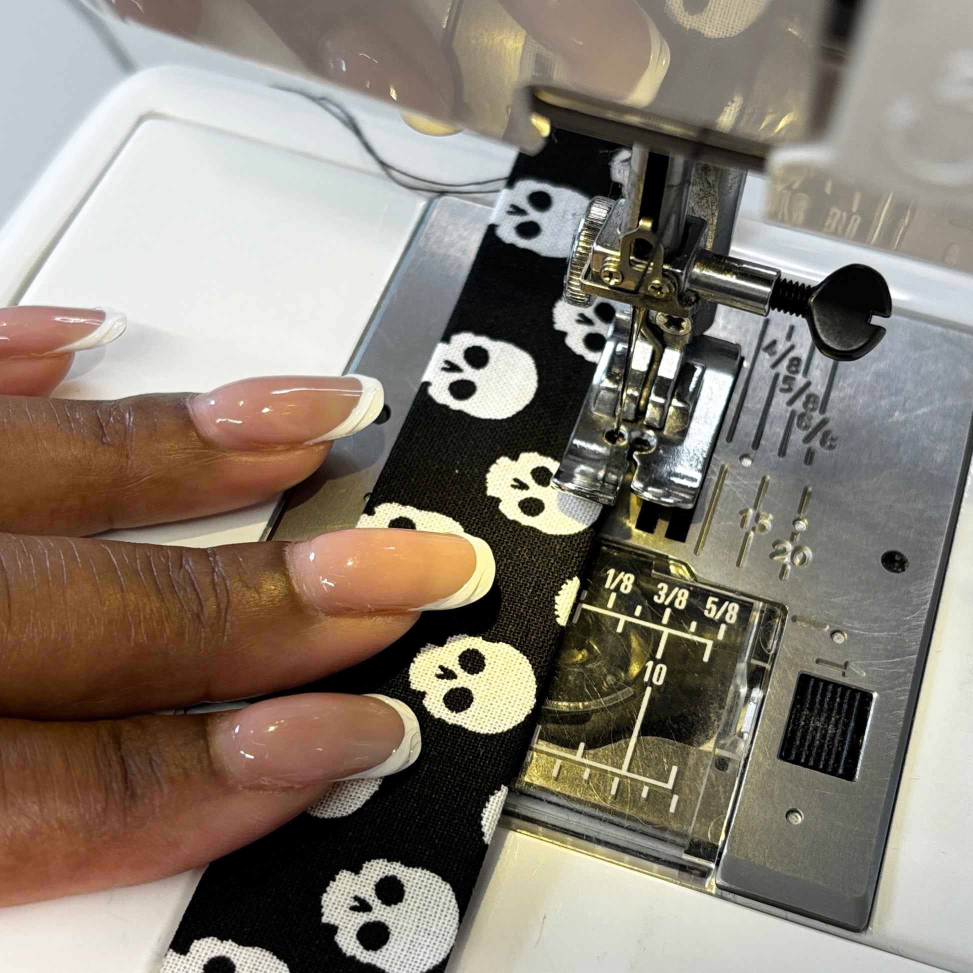 Sewing machine needle stitching a black fabric with white skull patterns.
