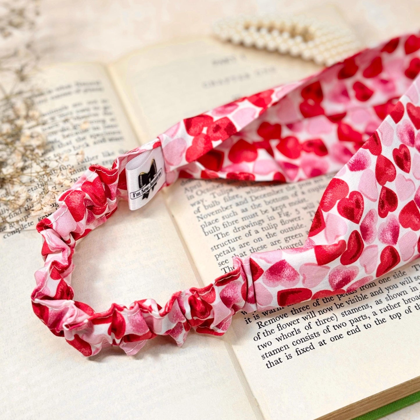 Cotton heart print pink and red headband thick, flat, wide stretch on top of book open pages, showcasing close-up detail of the back elastic ruffle, perfect for hair styling and fashion accessories, from a small business.