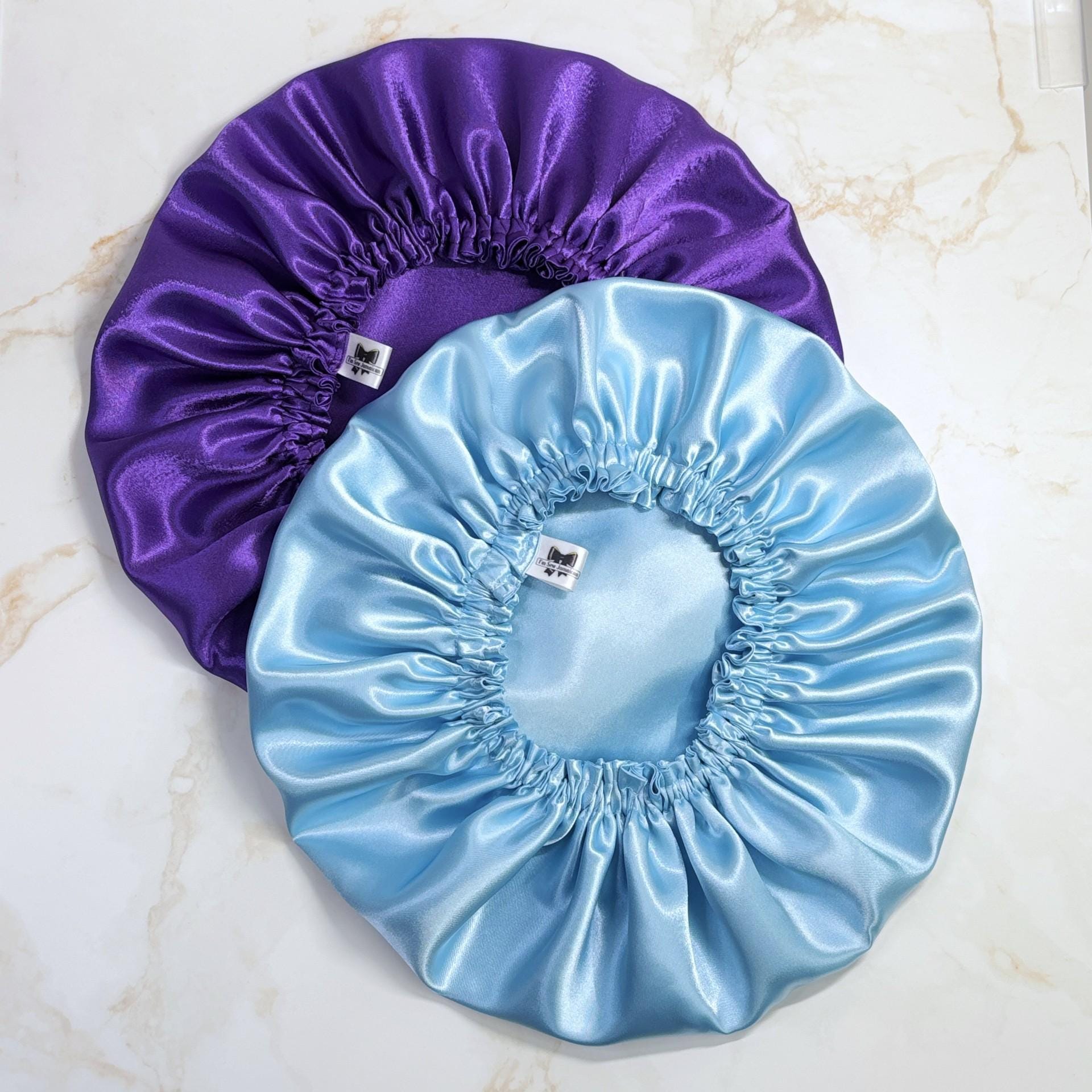 Purple and baby blue satin bonnets on a marbled background, perfect for hair care, night protection.