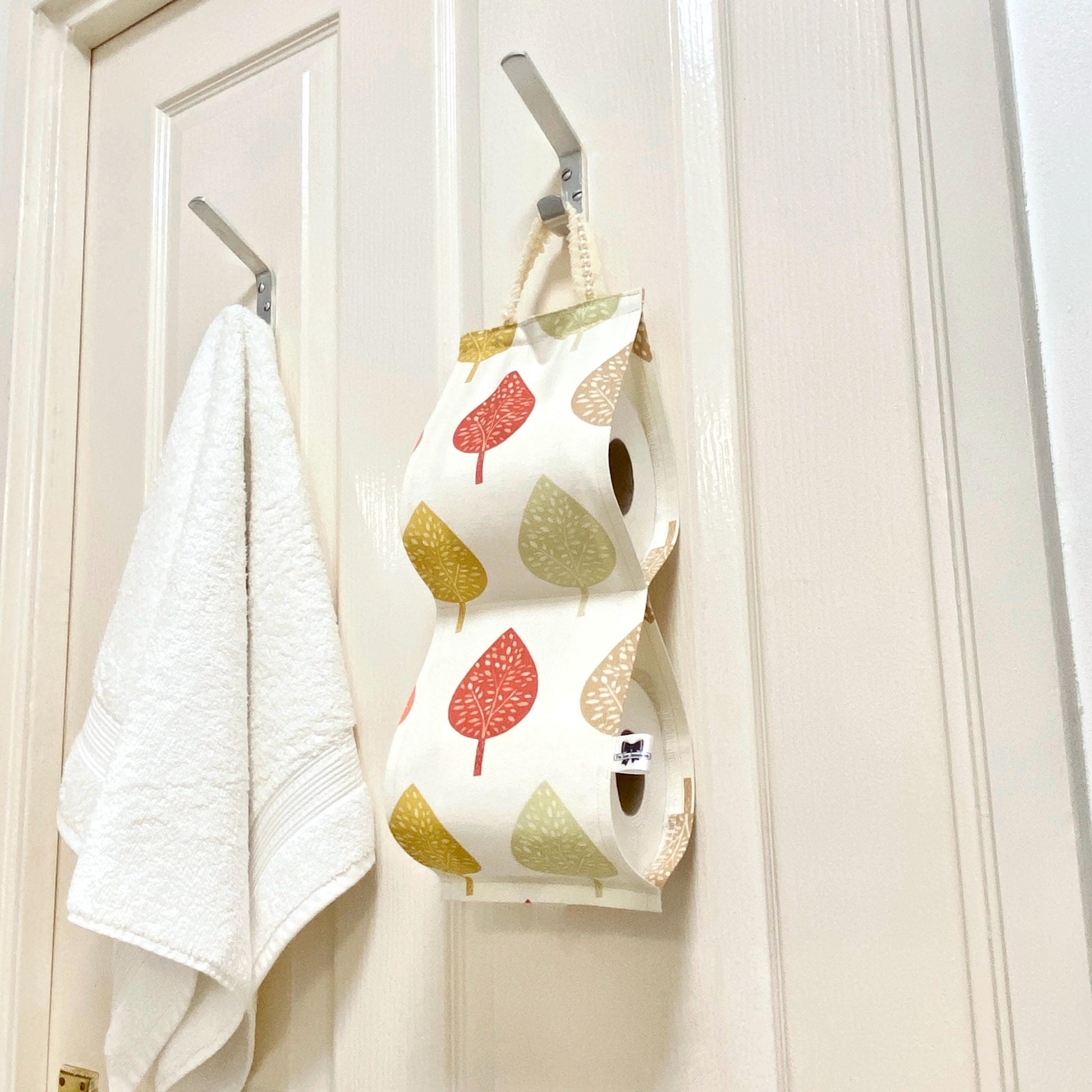 Earthy cotton fabric toilet roll holder with leaves, hanging in a bathroom.