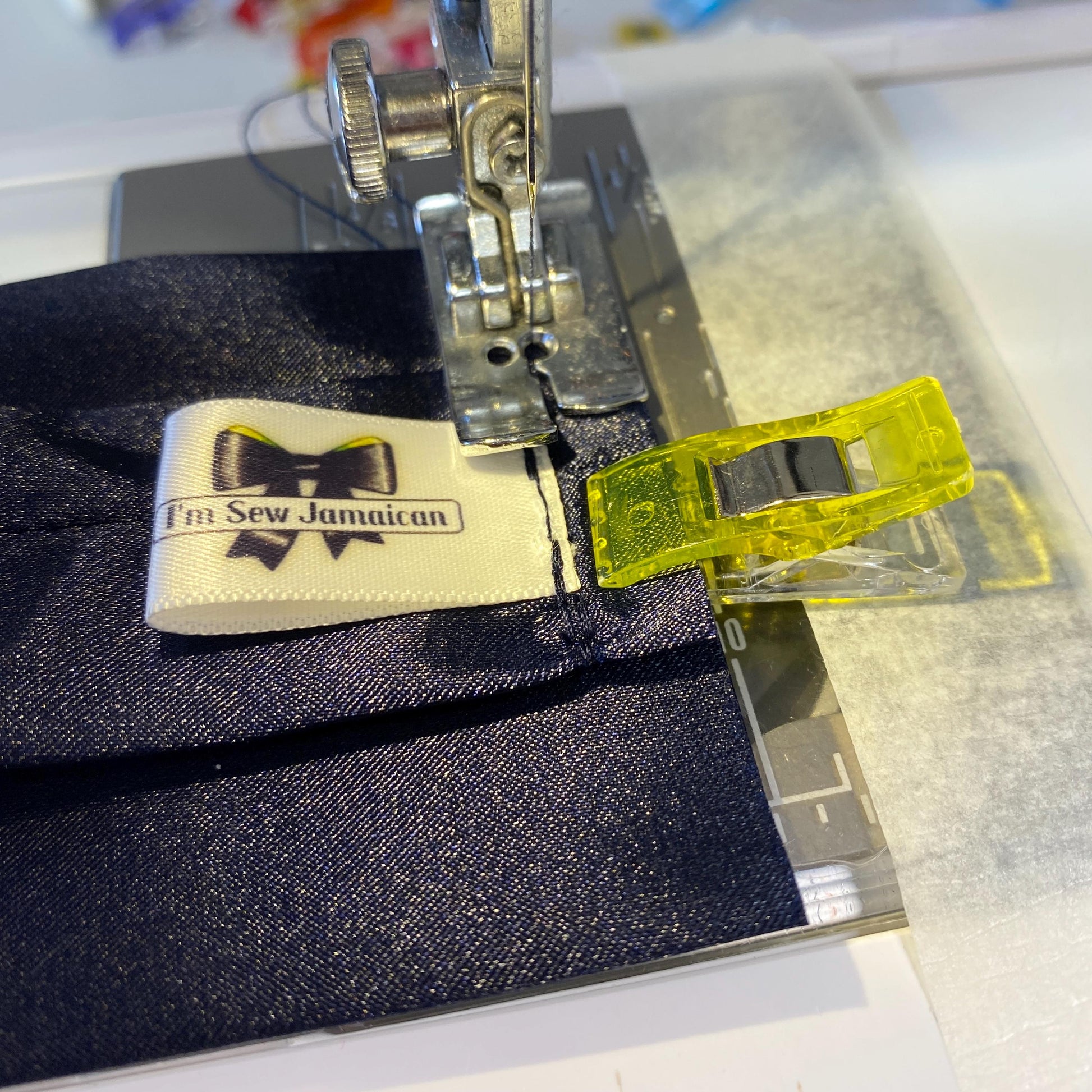 Close-up of a sewing machine stitching a navy blue satin headband, with the needle in focus.