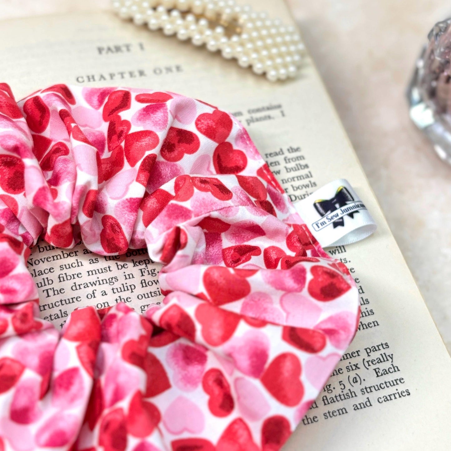 Close up of cotton heart scrunchie placed on top of a book in flat lay.