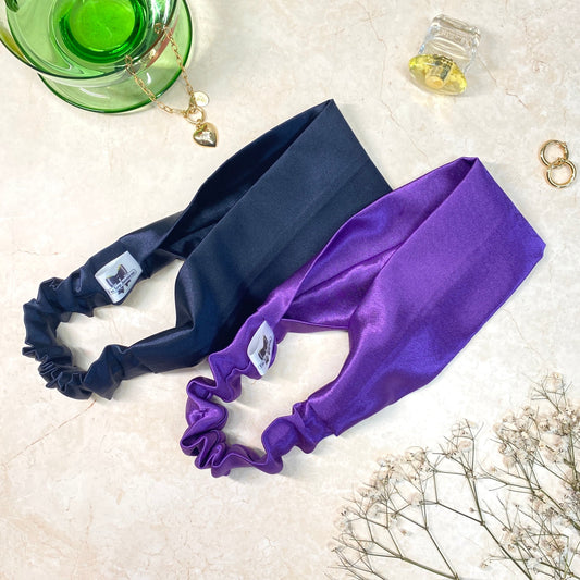 Thick, wide, flat navy blue and purple satin headbands with an elastic back, displayed on a marble background.