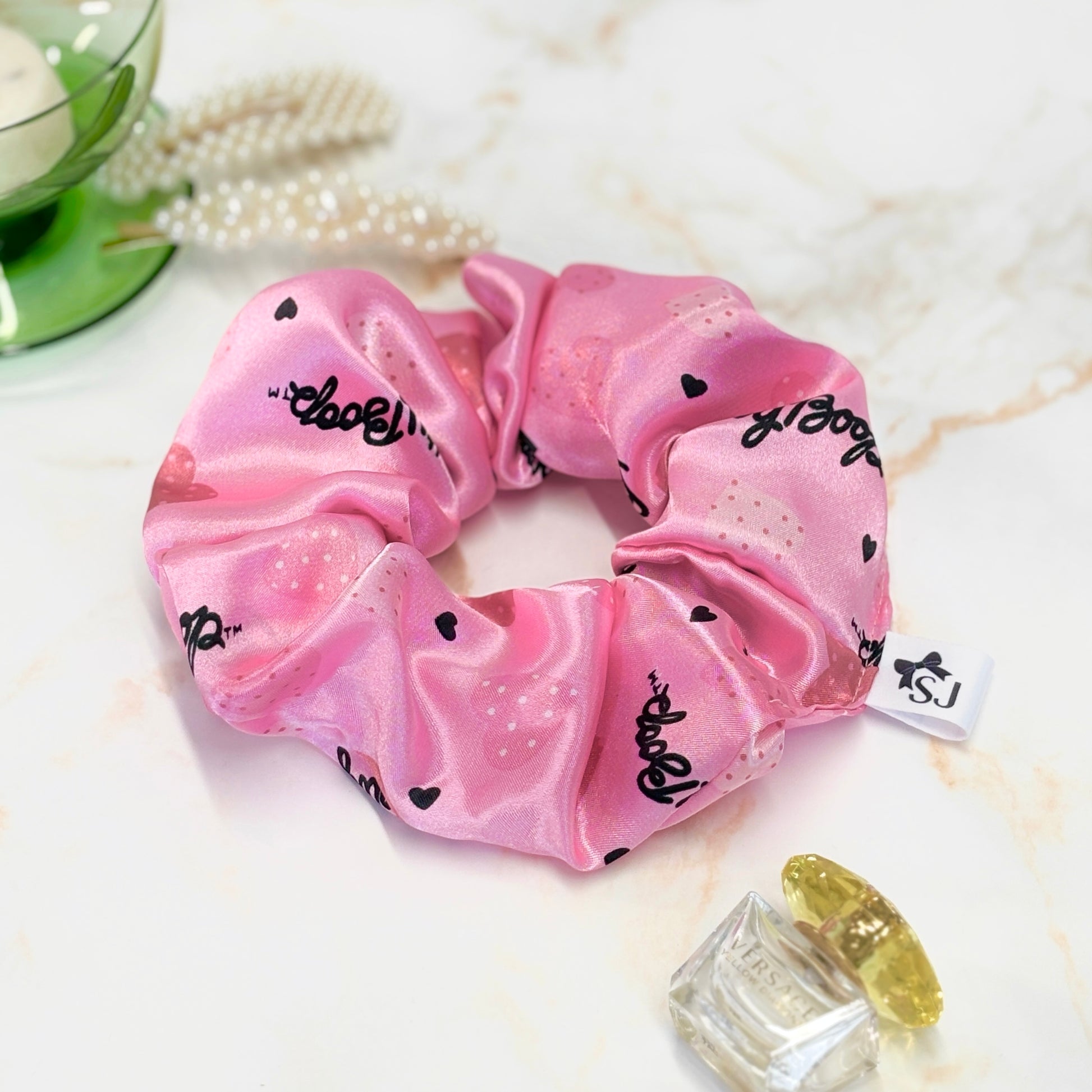 Close up pink Betty Boop satin scrunchie in a flat lay with props, including hair accessories and perfume.