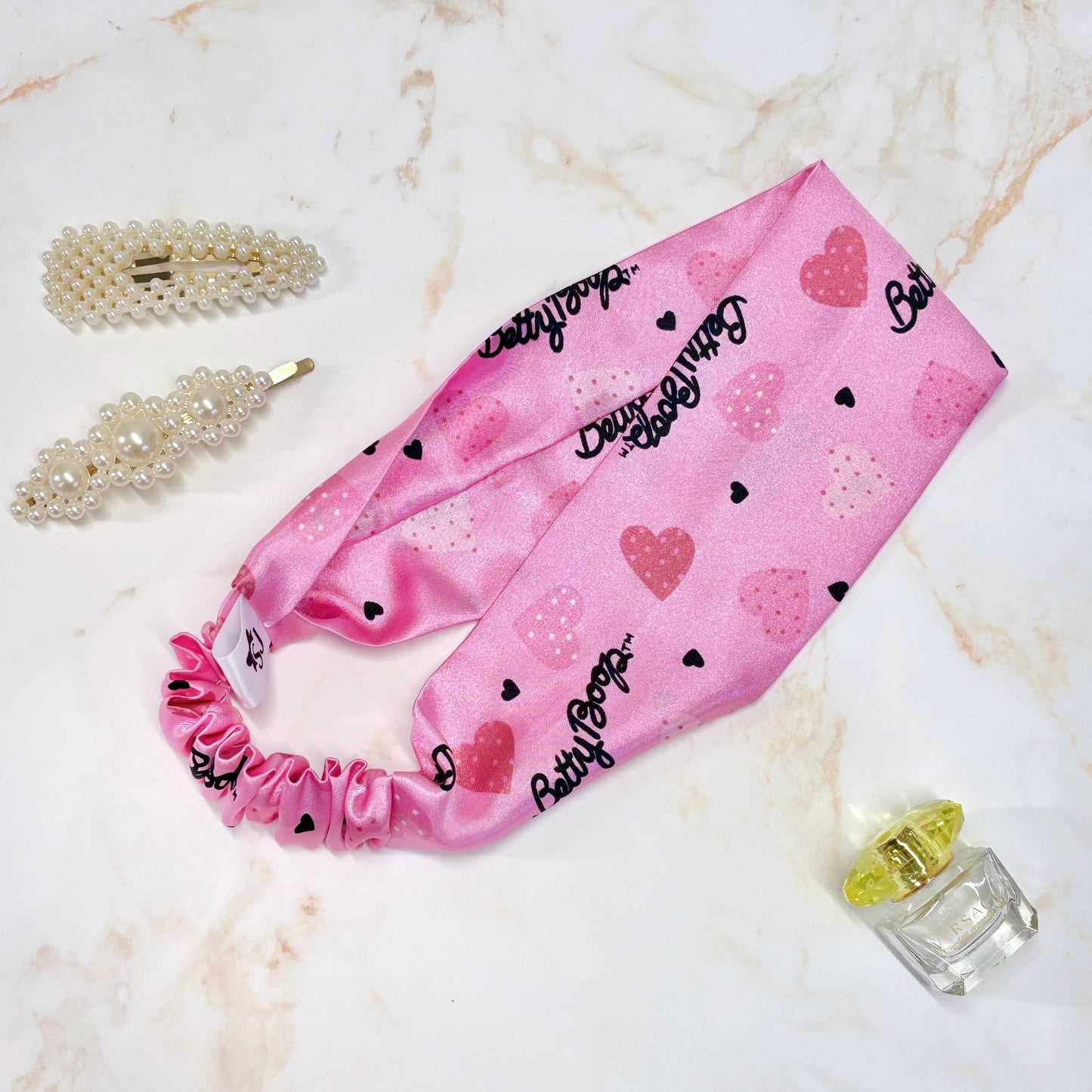 Pink Betty Boop thick wide flat headband in a flat lay with hair accessory and perfume props
