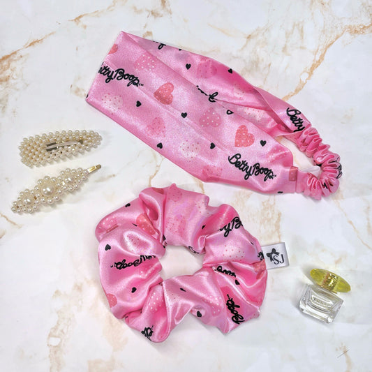 Betty Boop pink satin hair scrunchie and pink satin headband displayed on a marble background with props.
