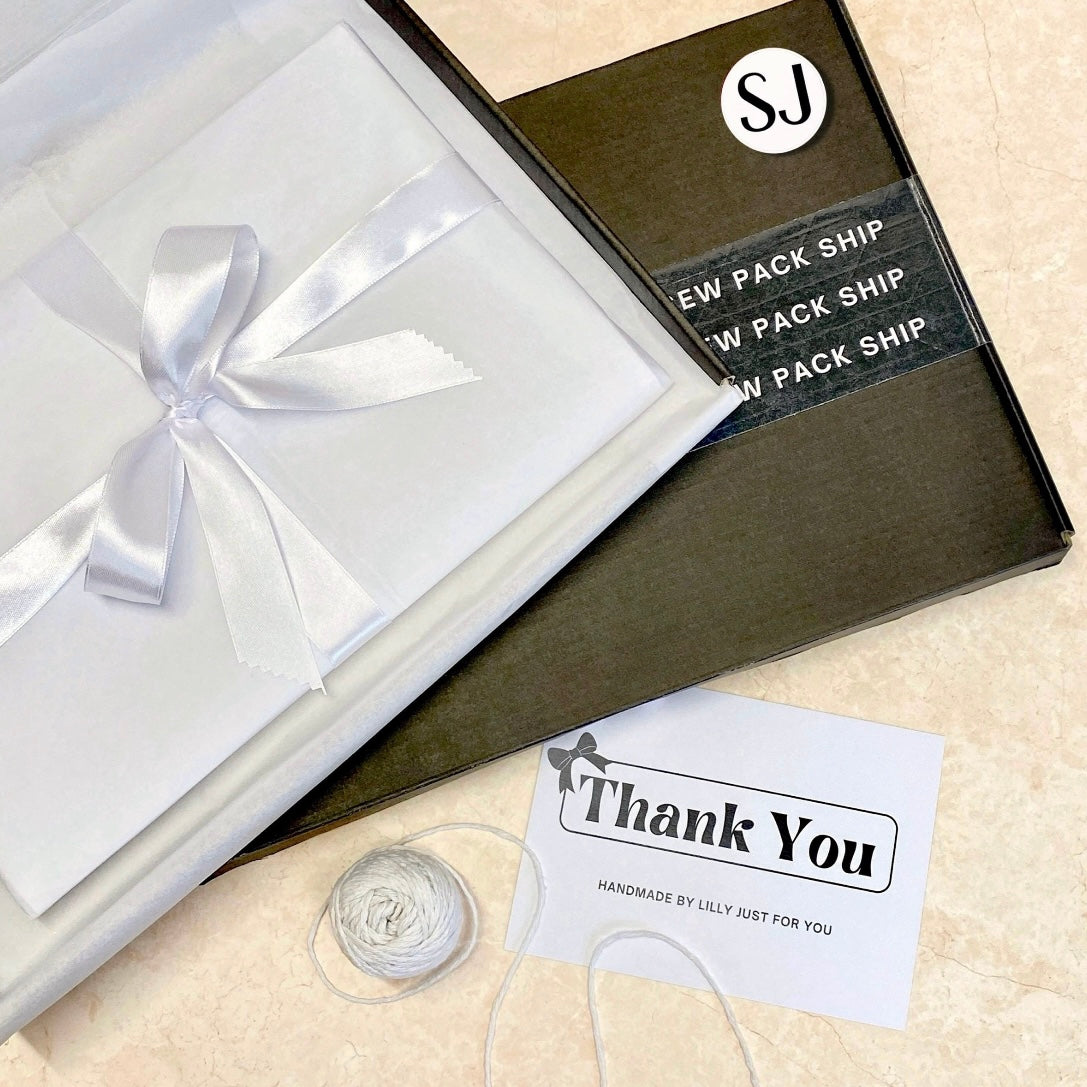 Small business gift packaging with white tissue wrap, white satin bow ribbon, thank you card reading “Handmade by Lilly just for you” inside a branded postal box.