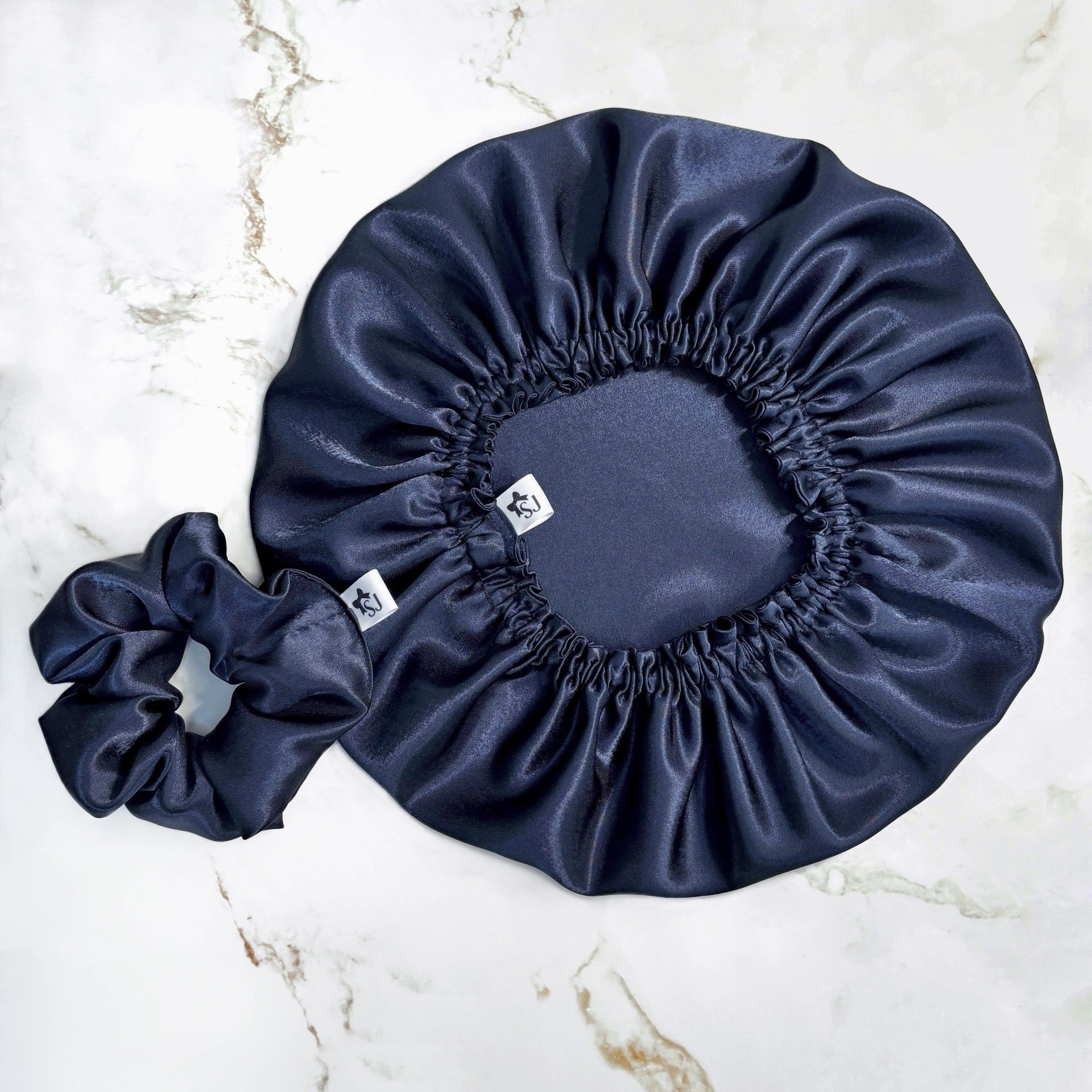Navy blue satin bonnet and matching scrunchie on a marble surface