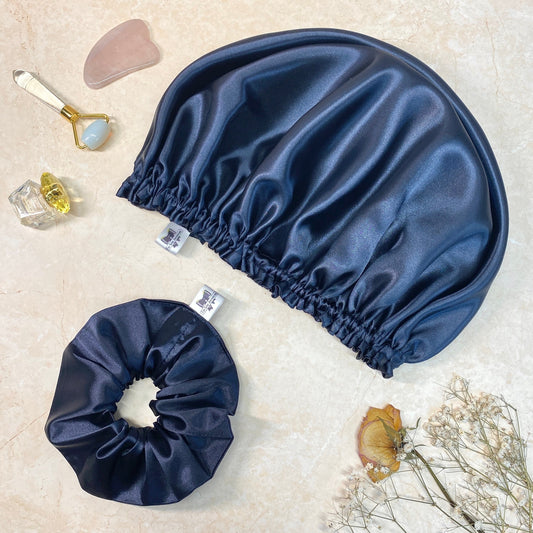 Navy blue satin hair bonnet for protecting hair and hair scrunchie  displayed on a marble background.
