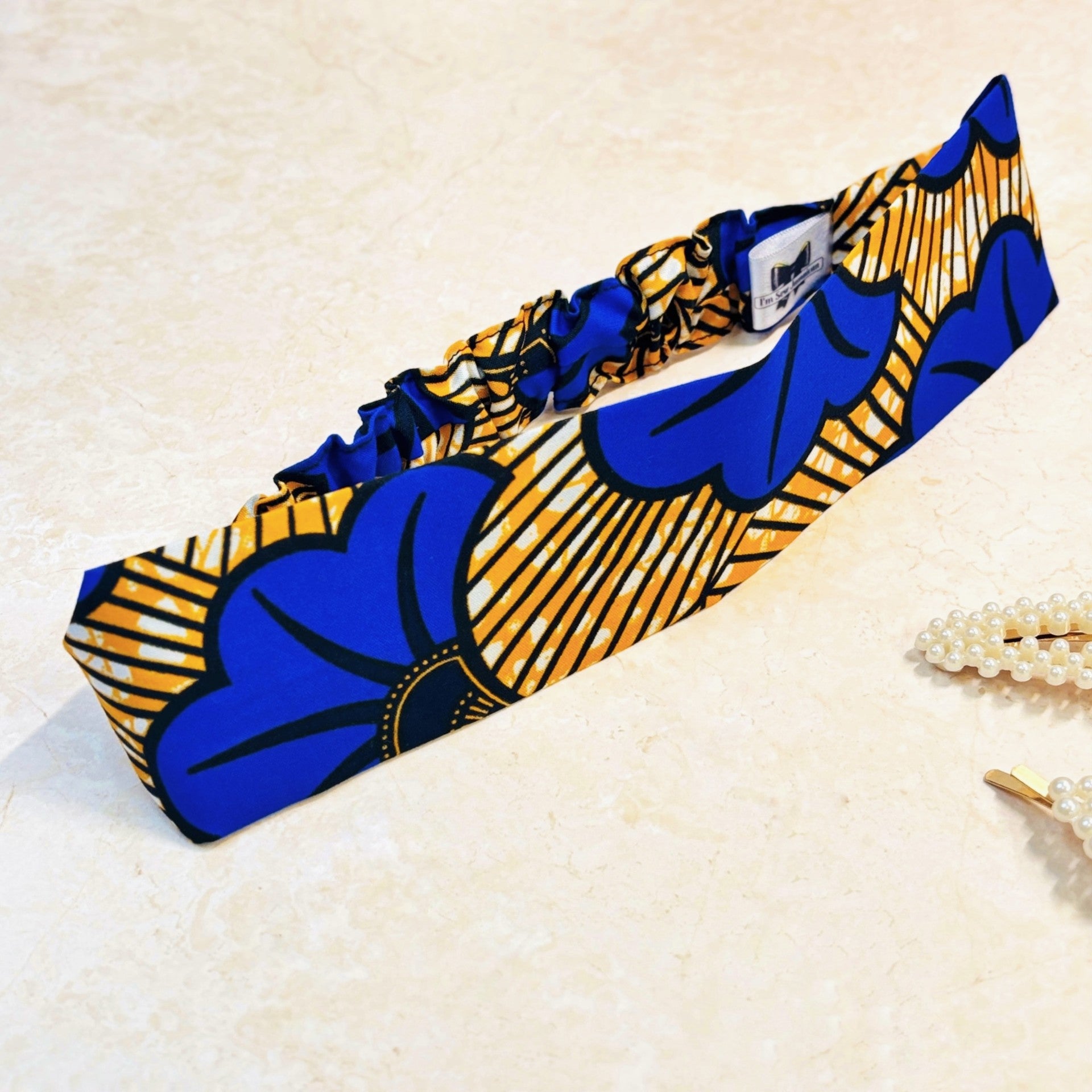 Floral print blue and yellow thick, flat, wide stretch headband on a peach background with props.