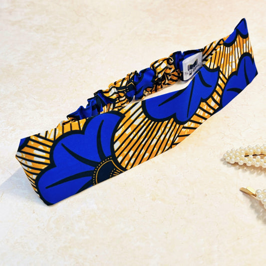Floral print blue and yellow thick, flat, wide stretch headband on a peach background with props.