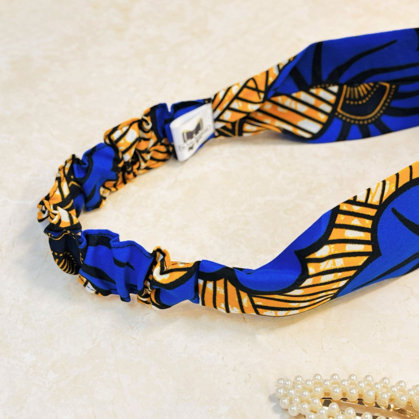 Floral print blue and yellow thick, flat, wide stretch headband on a peach background with props.