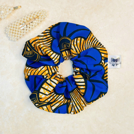 Blue and yellow African print scrunchie on a peach background with hair clips, perfect for hair styling, fashion accessories, and adding vibrant colours, from a small business.