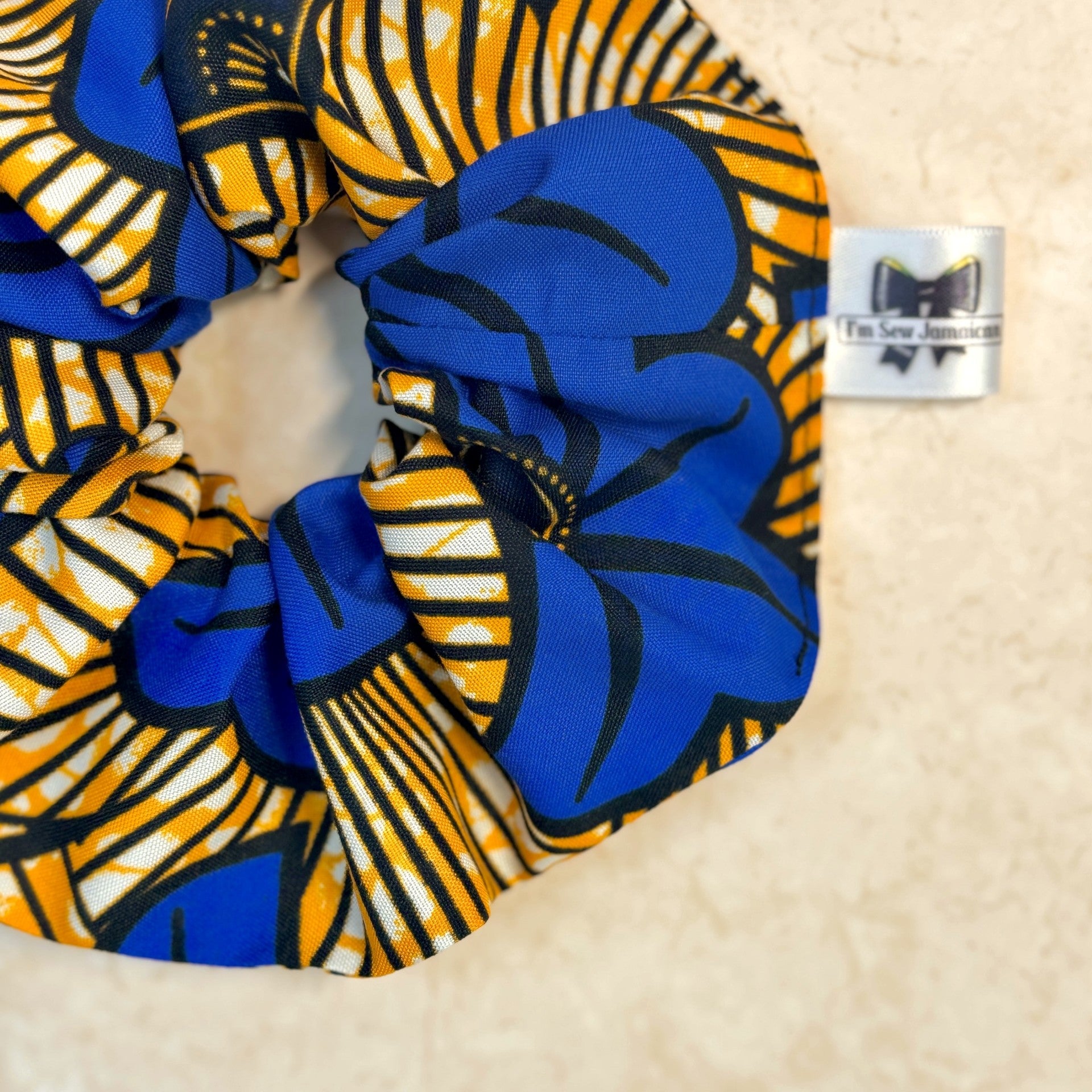 Close up of floral African print blue and yellow scrunchie displayed on marble background.