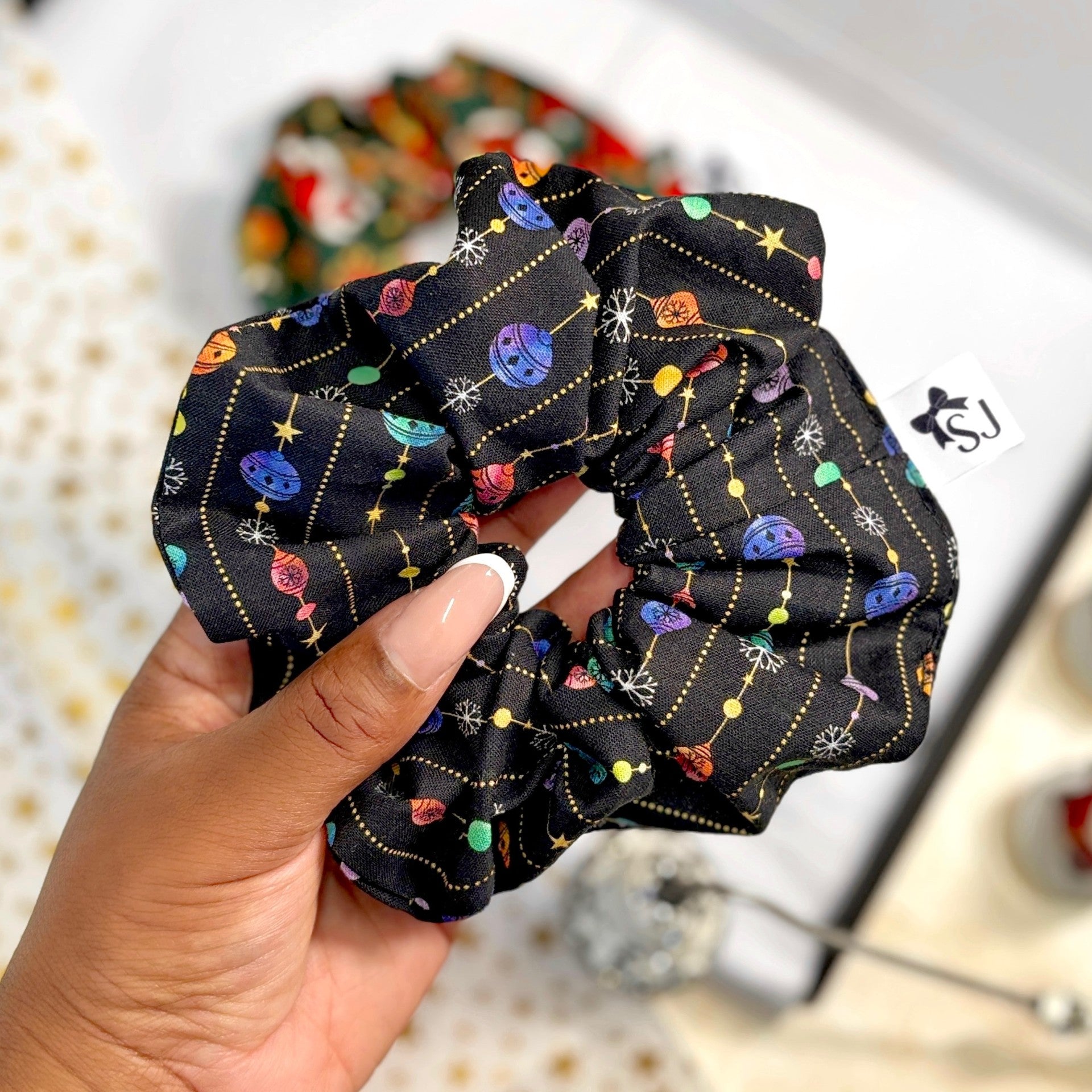 Black Christmas scrunchie held by a hand against a blurred background