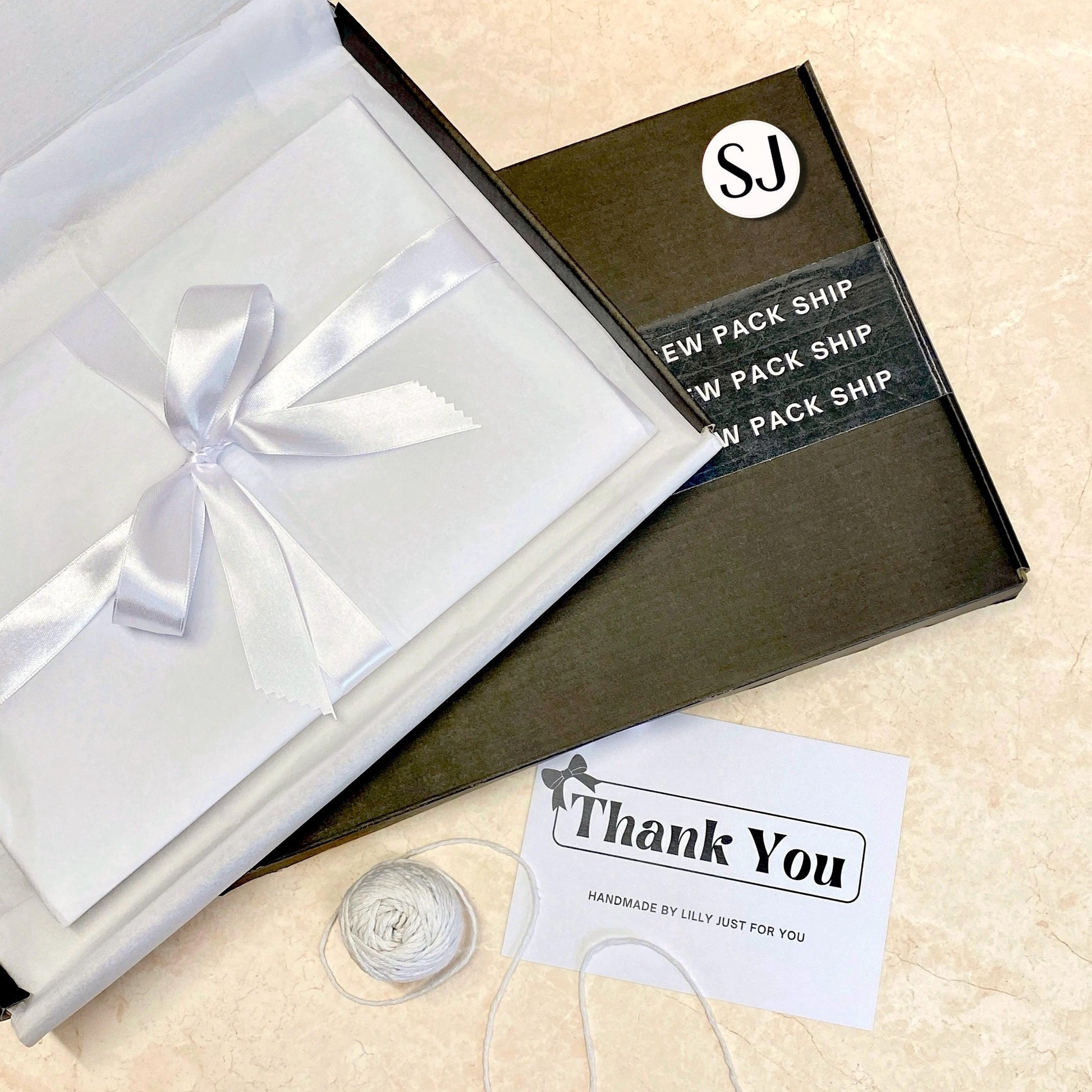 Small business gift packaging with white tissue wrap, white satin bow ribbon, thank you card reading “Handmade by Lilly just for you” inside a branded postal box.