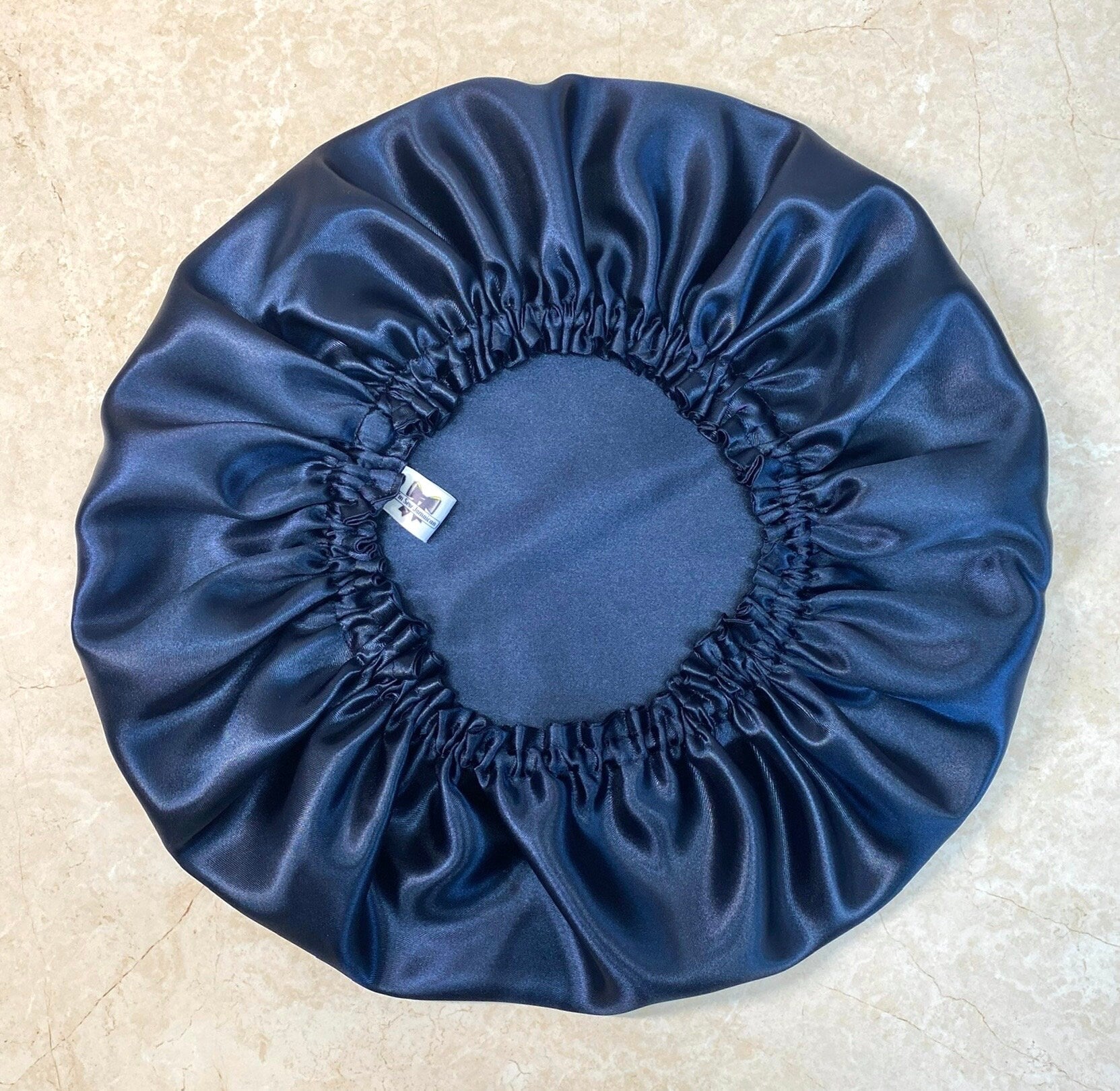 Navy blue satin hair bonnet for protecting hair, displayed on a marble background.
